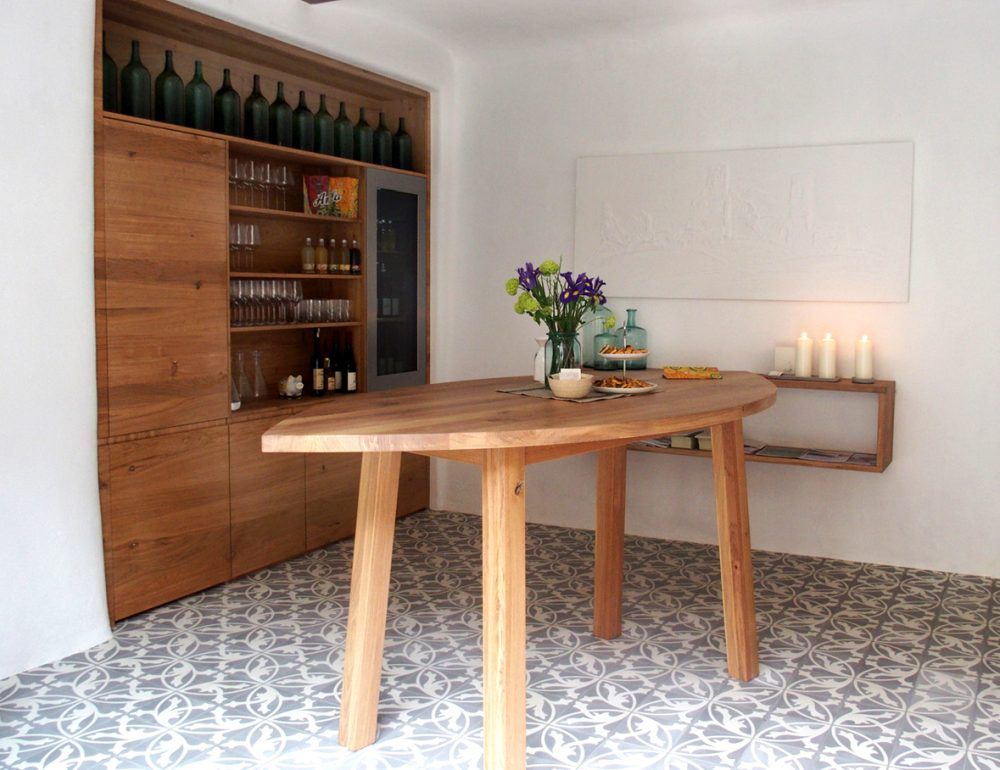 Ein stilvoller Verkostungsraum mit Holztisch, Regal mit Flaschen und Gläsern, Blumen und Kerzen.