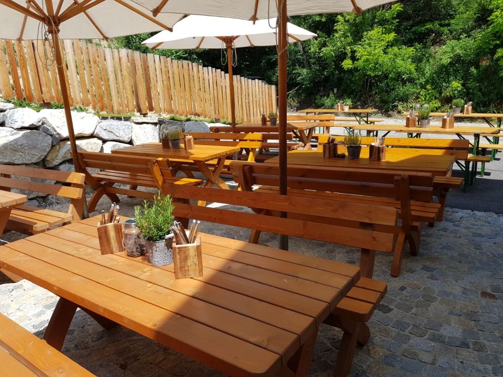 Holzbänke und Tische im Freien mit Sonnenschirmen und Pflanzen.