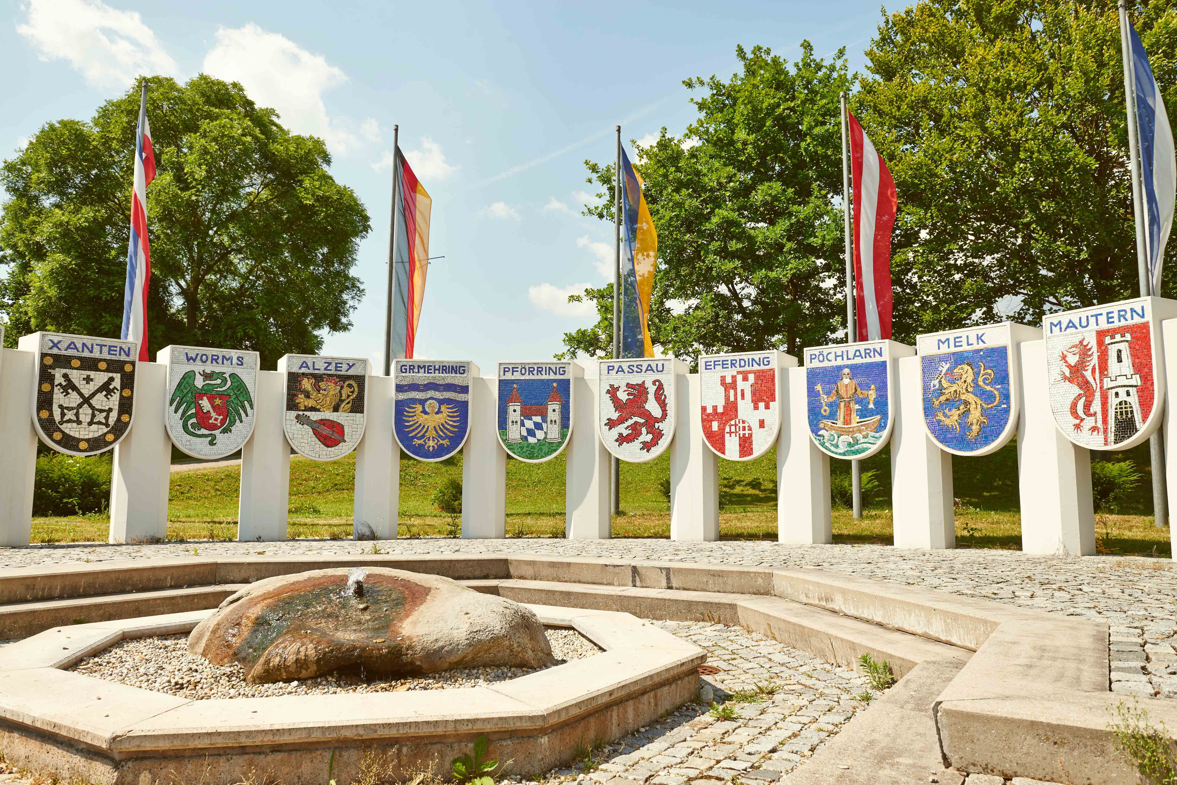 Nibelungendenkmal mit Wappen verschiedener Städte und Flaggen im Hintergrund.