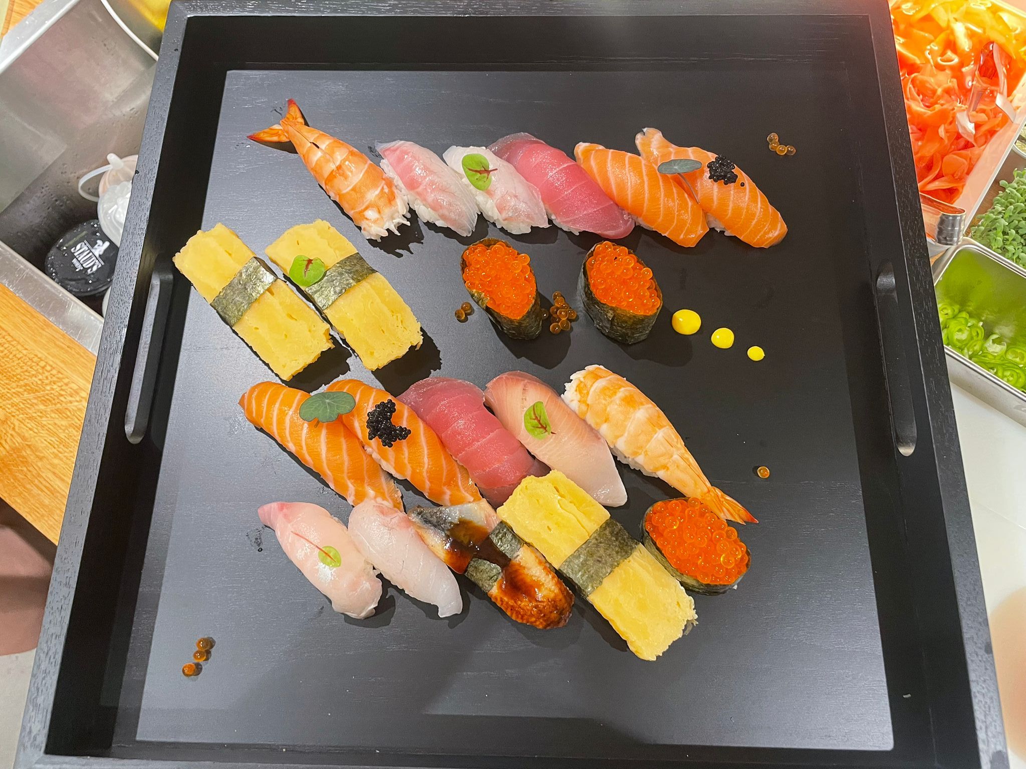 Ein schwarzes Tablett mit einer Auswahl an Sushi, darunter Nigiri und Maki, dekoriert mit Kaviar und Kräutern.
