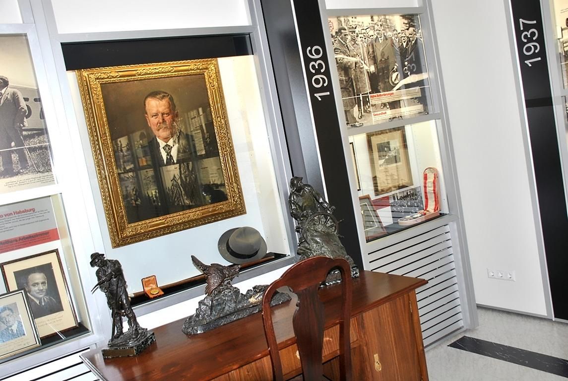 Innenansicht eines Museums mit Gemälden, Skulpturen und historischen Fotos.