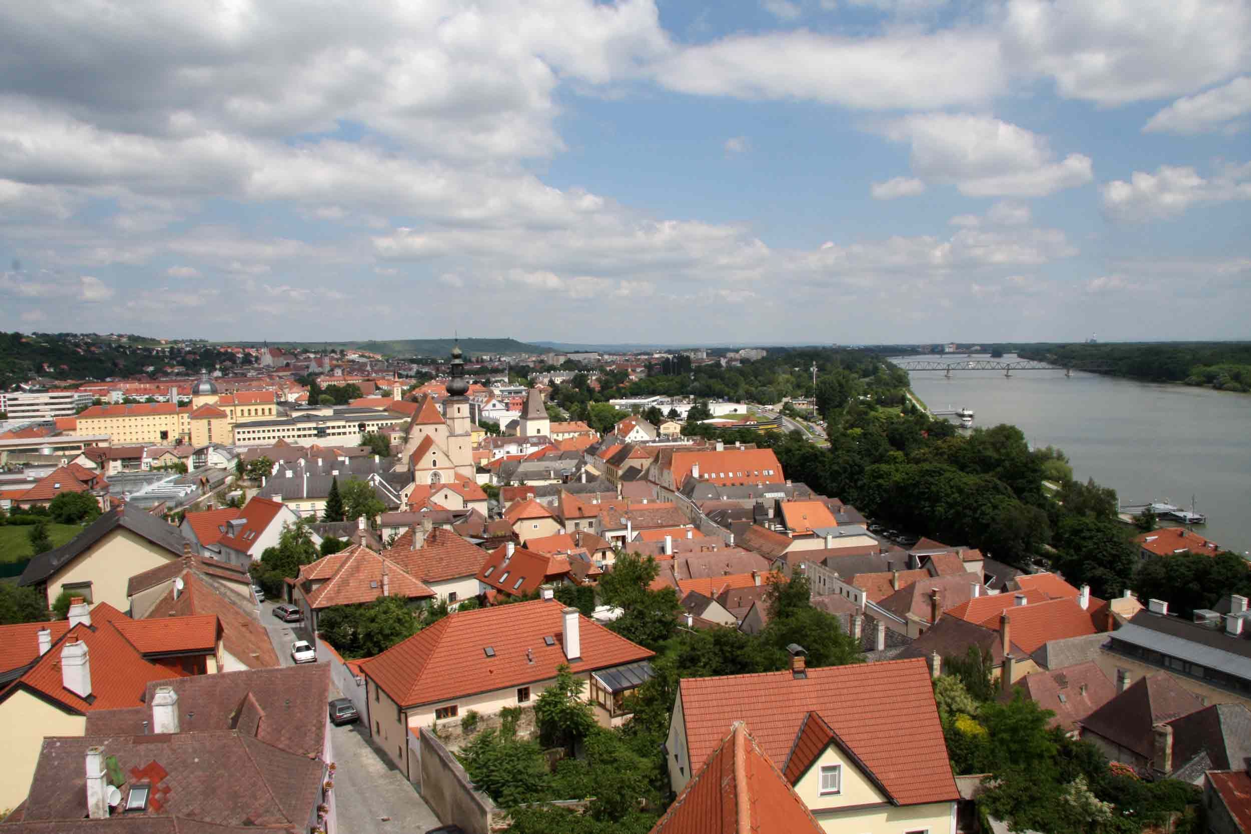 Panoramatický pohled na střechy Kremže s řekou a mostem v pozadí.