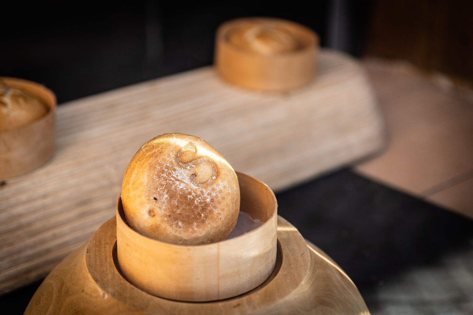 Ein frisch gebackenes Wachauer Laberl ruht in einem traditionellen Dampfgarer, umgeben von warmem Holz. Der verführerische Duft von frisch gebackenem Brot erfüllt die Luft und lädt dazu ein, die köstliche Spezialität zu probieren. Diese Delikatesse ist ein wahrer Genuss für alle, die die lokale Backkunst schätzen.