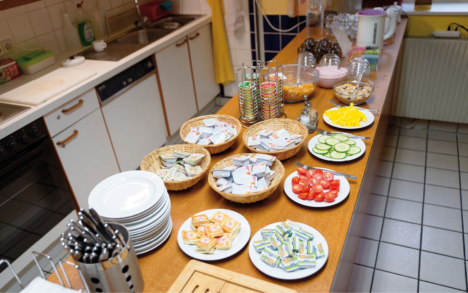 Frühstücksbuffet mit Tellern, Besteck, Aufstrichen, Gemüse und Müsli.
