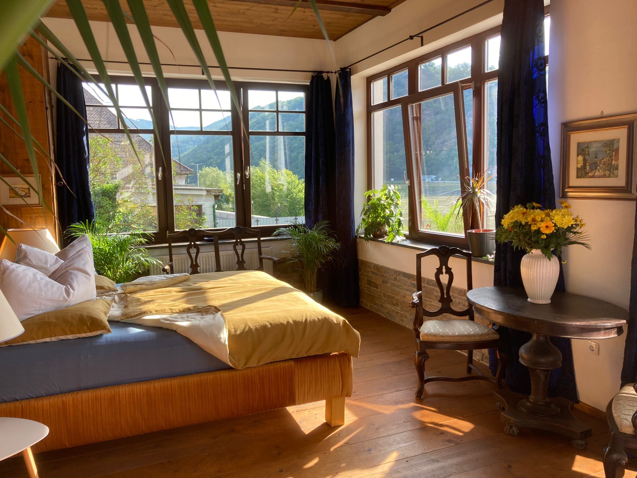 Gemütliches Schlafzimmer mit großen Fenstern, Pflanzen und antiken Möbeln.