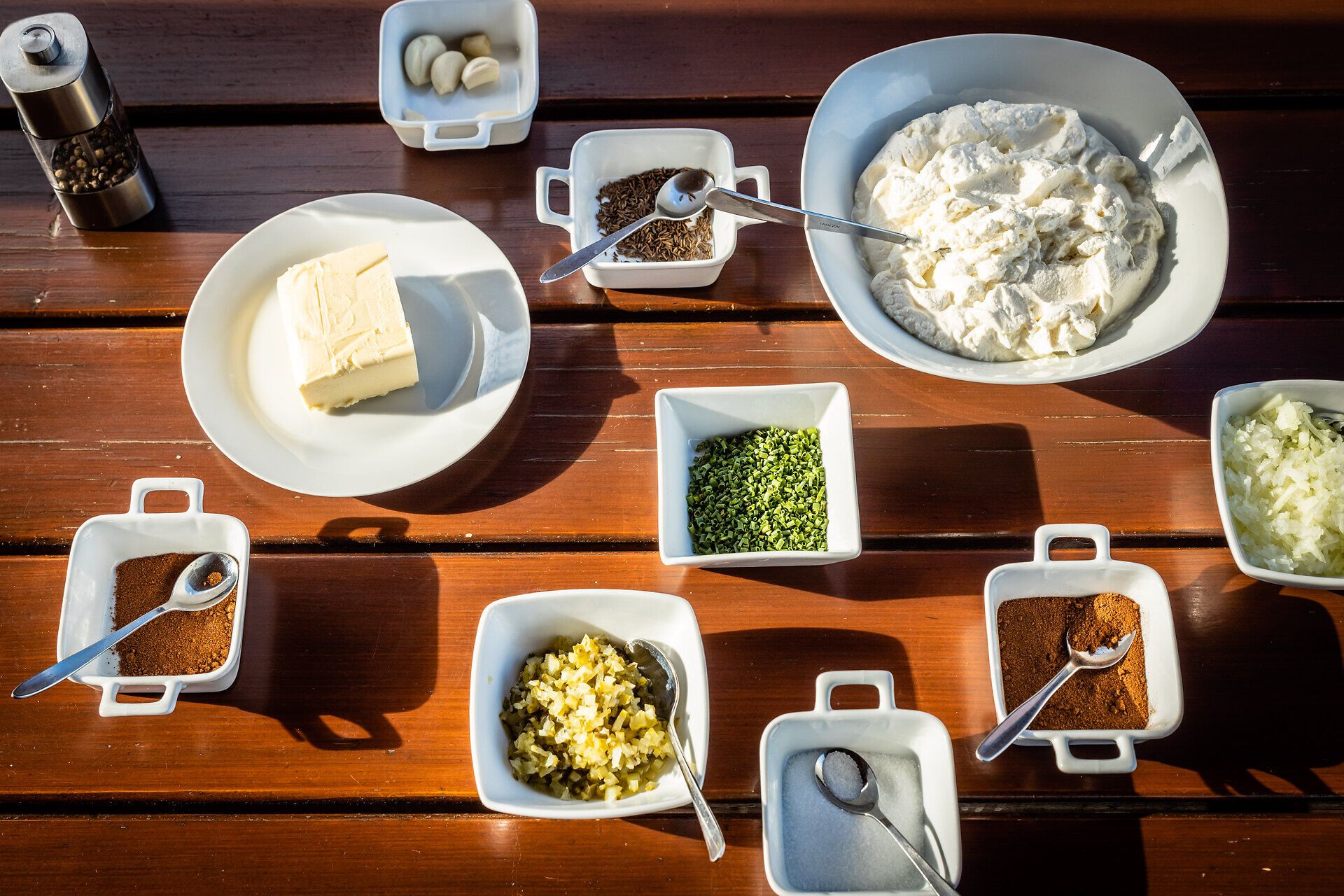 Eine einladende Auswahl an frischen Zutaten liegt auf einem rustikalen Holztisch, bereit für die Zubereitung einer köstlichen Speise. Die harmonische Anordnung von Kräutern, Gewürzen und cremigem Käse verspricht ein Geschmackserlebnis, das die Sinne verführt und die Vorfreude auf ein geselliges Beisammensein weckt.