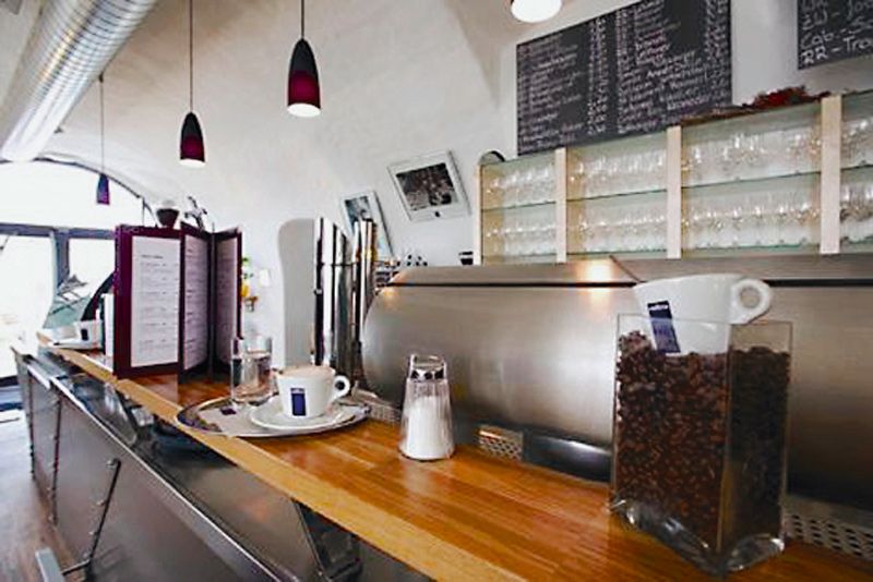 Innenansicht eines Cafés mit Theke, Kaffeemaschine und Gläsern.