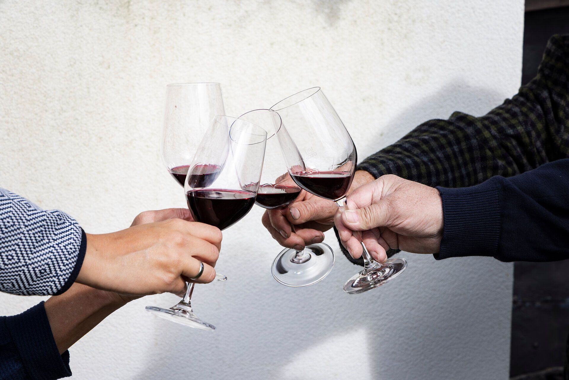 Vier Weingläser mit Rotwein stoßen an, zu sehen sind nur die Hände.
