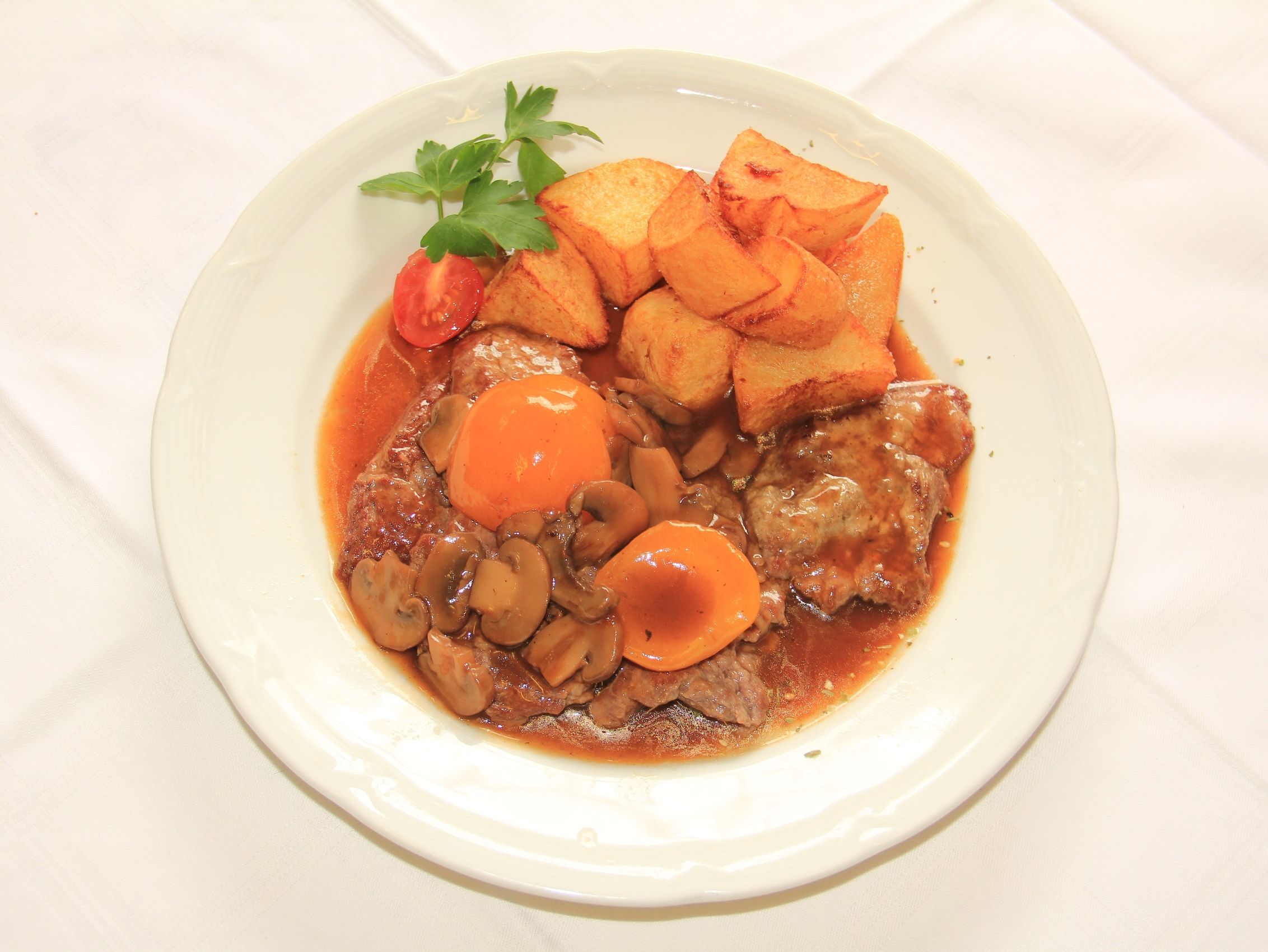 Ein Teller mit Wachauer Rostbraten, Pilzen und Bratkartoffeln.