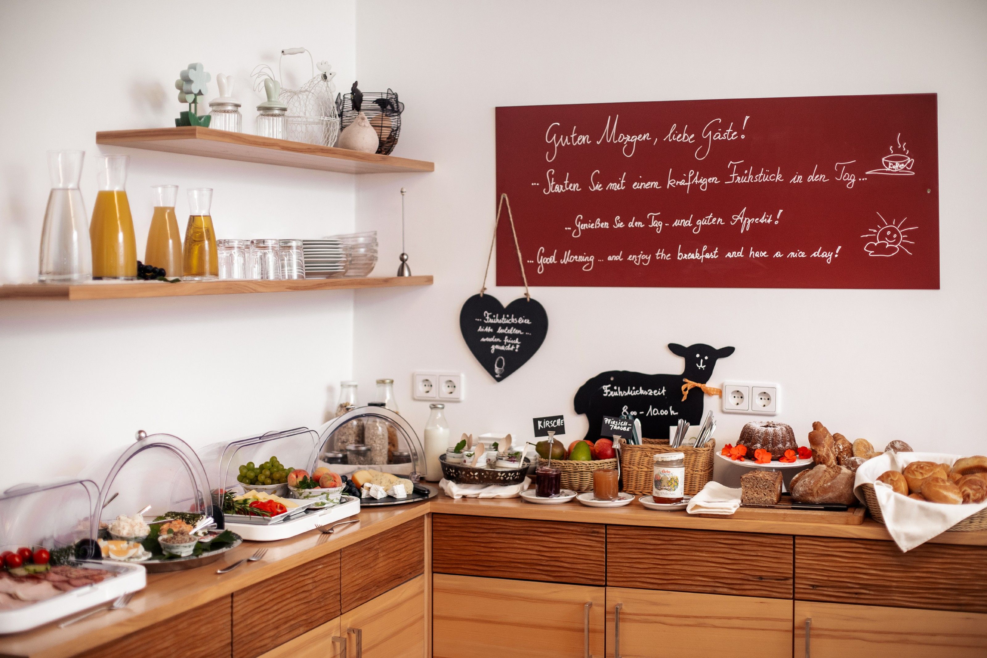 Frühstücksbuffet mit Saft, Brot, Aufschnitt und Obst in einem gemütlichen Raum.
