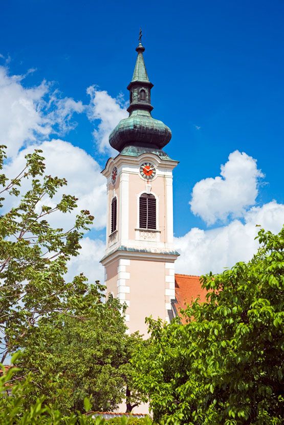 Turm einer Kirche mit Uhr und grünem Dach vor blauem Himmel.