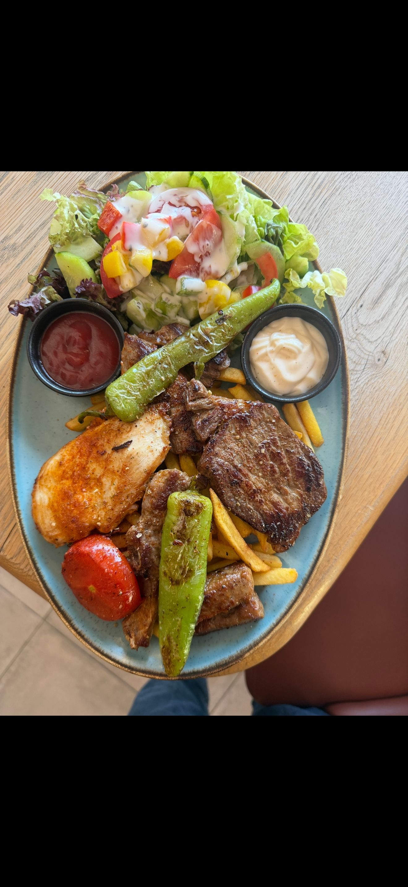 Egy tányér vegyes grillezett hús, chips, saláta és mártogatós.