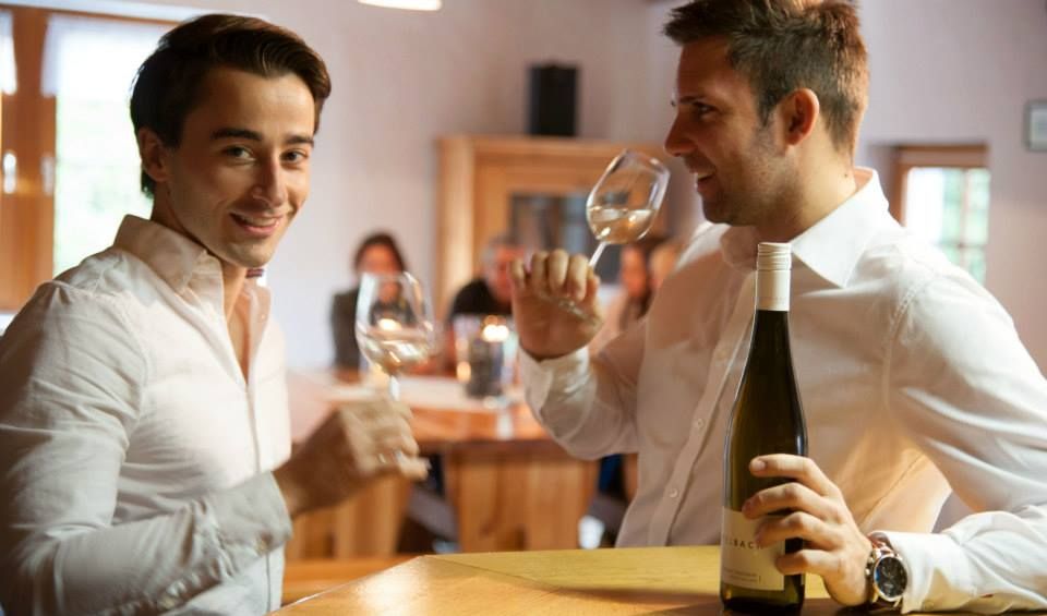 Zwei Männer in weißen Hemden trinken Wein in einem gemütlichen Raum.