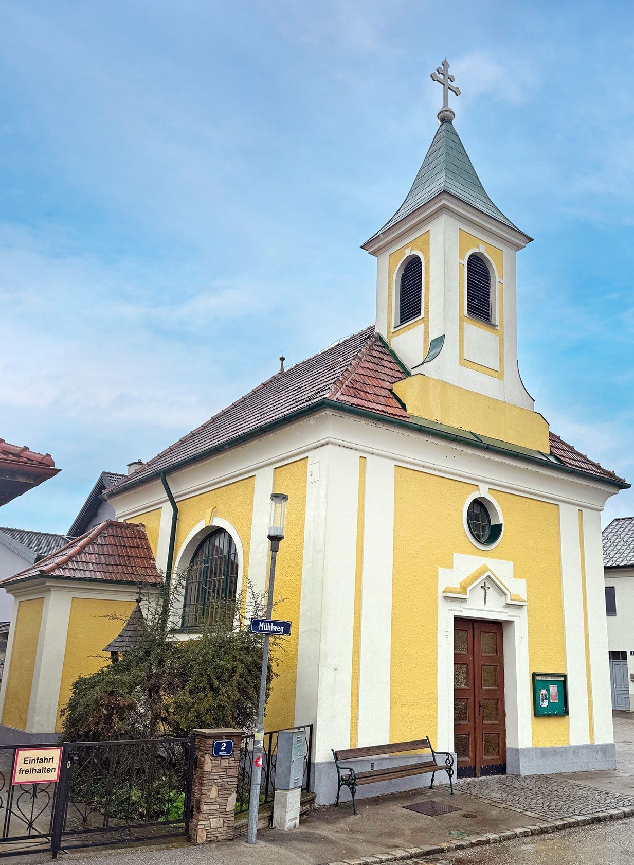 Yellow chapel with tower and cross in Oberzögersdorf, surrounded by blue sky.