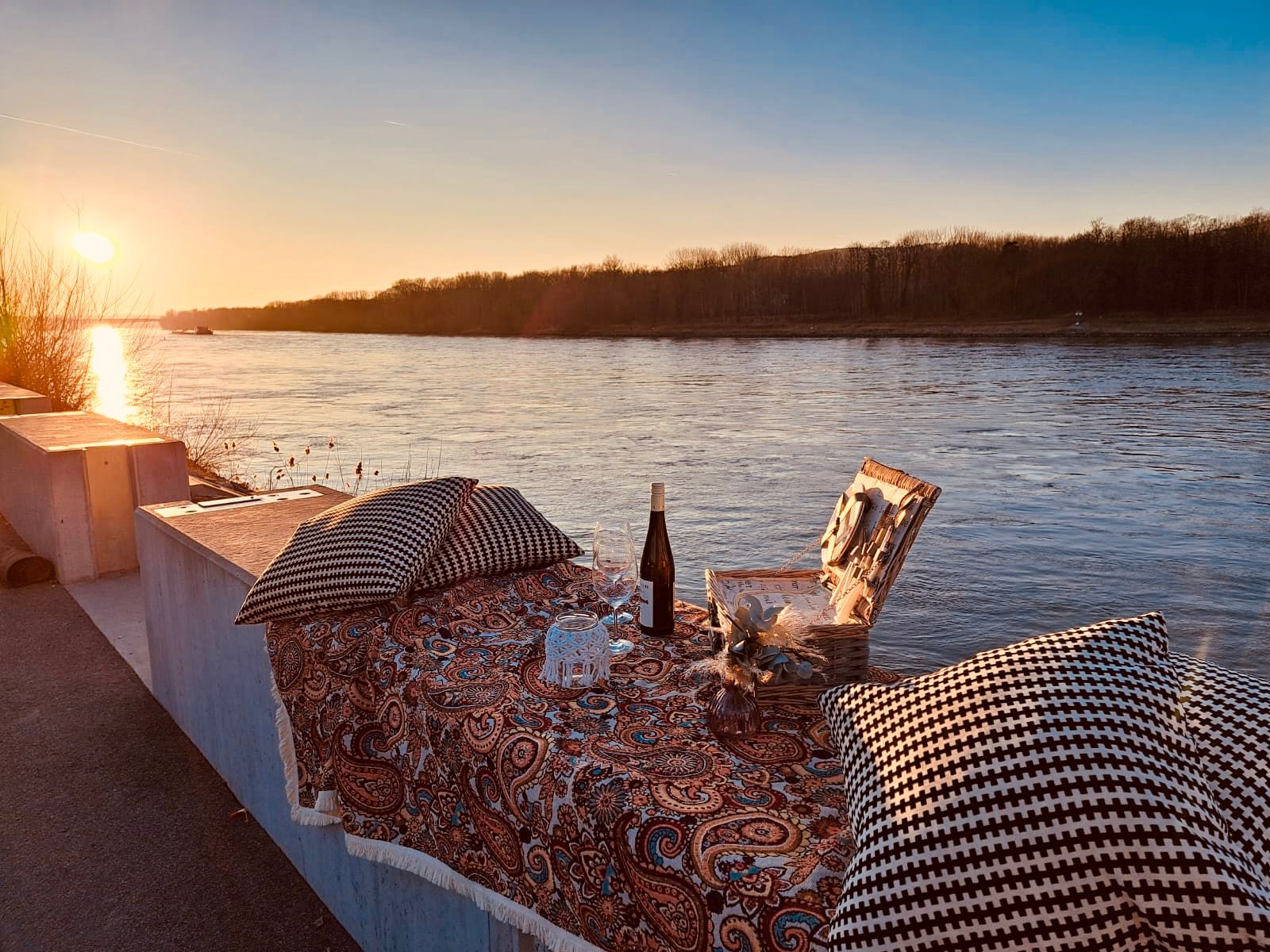 Picknick an der Donau bei Sonnenuntergang mit Wein und Kissen.