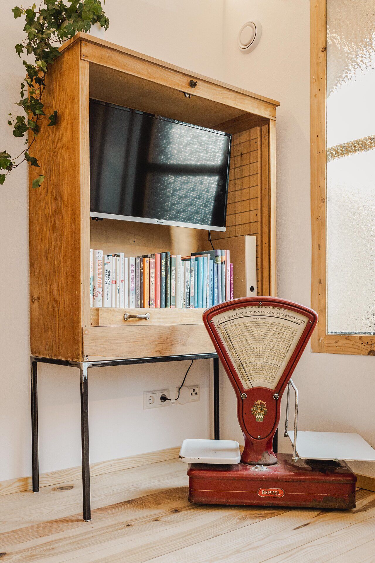 Offenes Holzregal mit Fernseher und Büchern, daneben eine alte Waage.