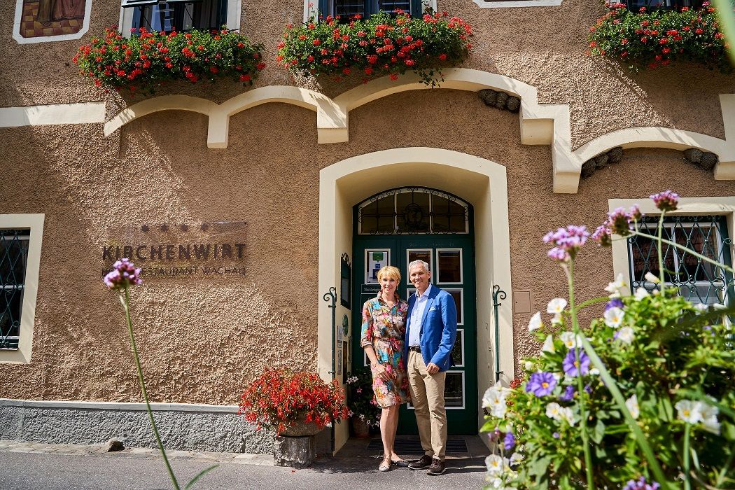 Familie Wildeis steht vor einem historischen Gebäude mit Blumen und der Aufschrift 'Kirchenwirt Restaurant Wachau'.
