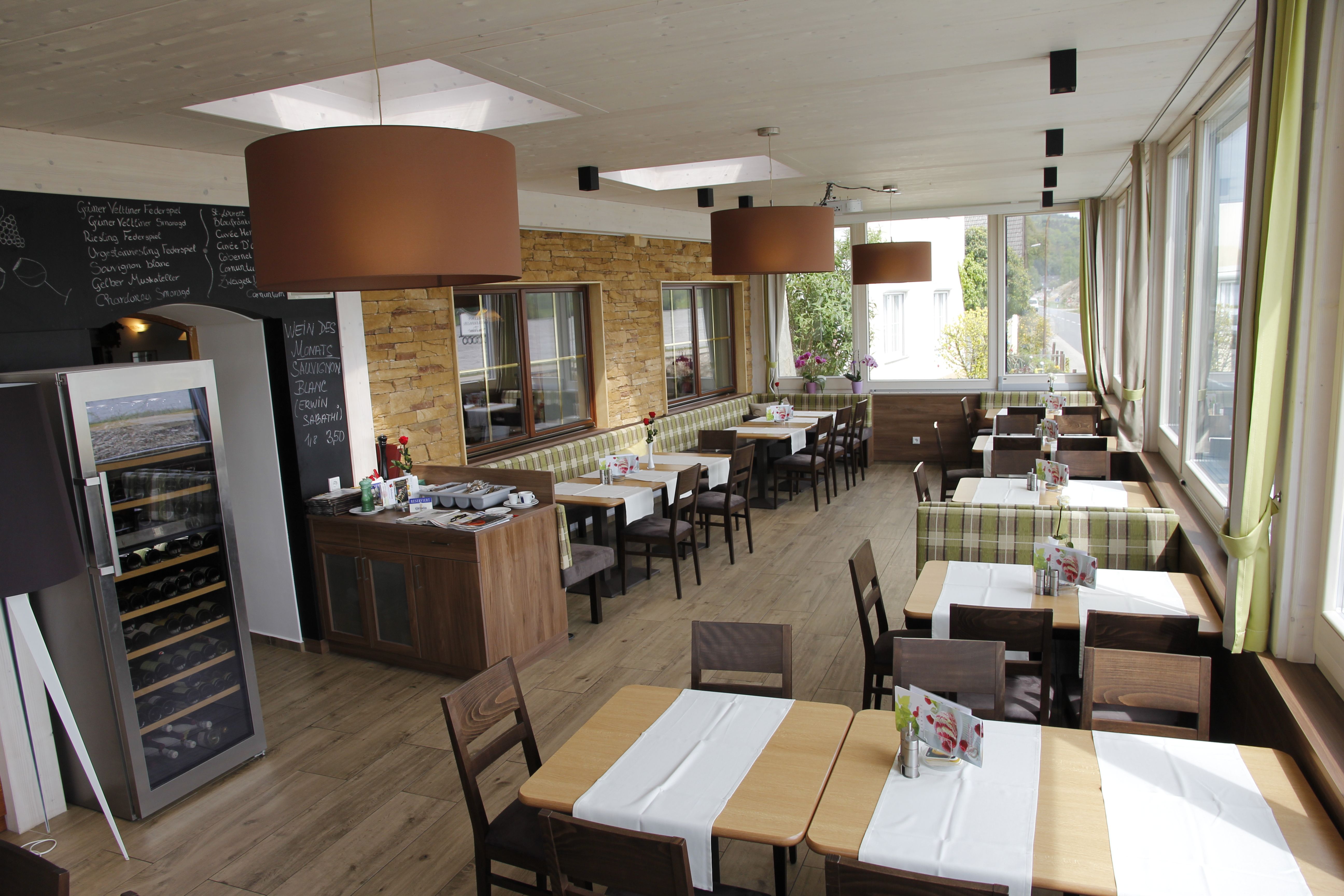 Innenansicht eines Wintergartens mit Tischen und Stühlen, großen Fenstern und moderner Dekoration.