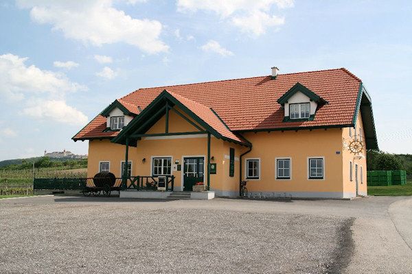 Ein gelbes Gebäude mit rotem Dach und grünen Akzenten, umgeben von einer ländlichen Landschaft.