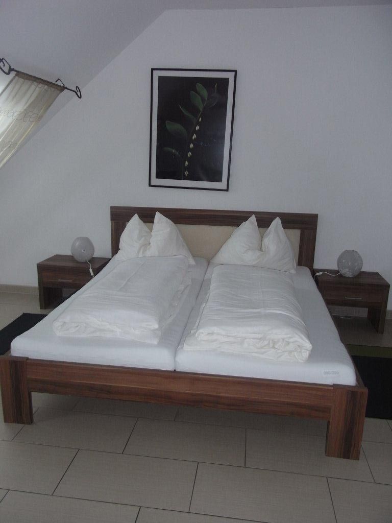 Ein schlicht eingerichtetes Schlafzimmer mit einem Doppelbett, zwei Nachttischen und einem Pflanzenbild an der Wand.