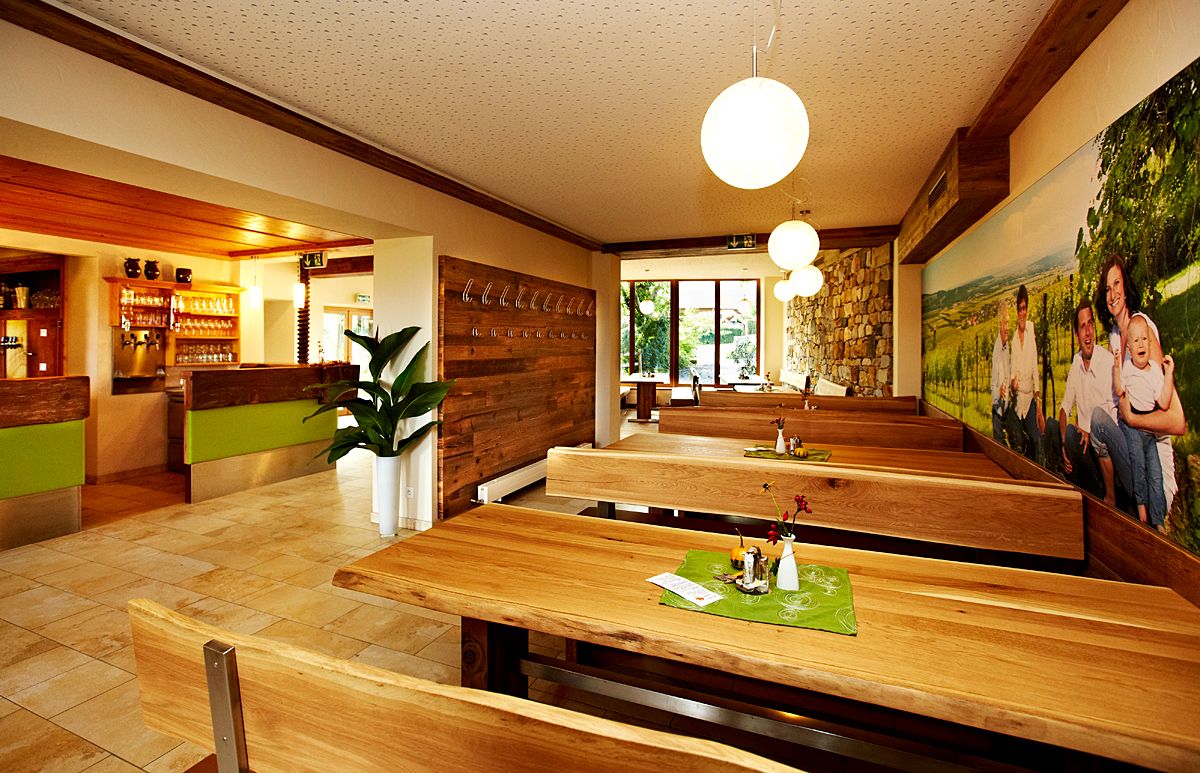 Innenansicht eines gemütlichen Restaurants mit Holztischen und -bänken, dekoriert mit Pflanzen und einem großen Wandbild.