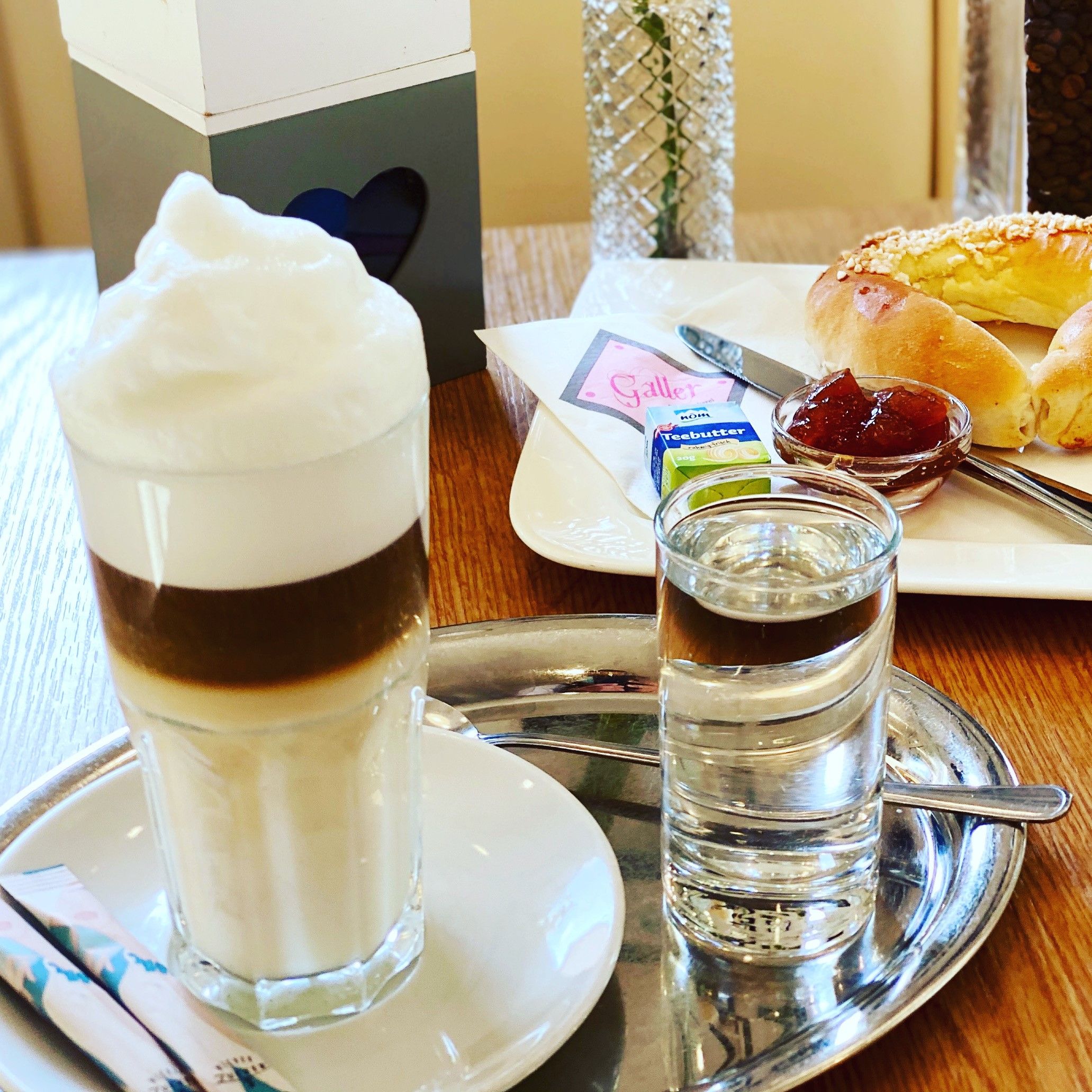 Gedeckter Frühstückstisch mit Latte Macchiato und Brioche Kipferl mit Marmelade 