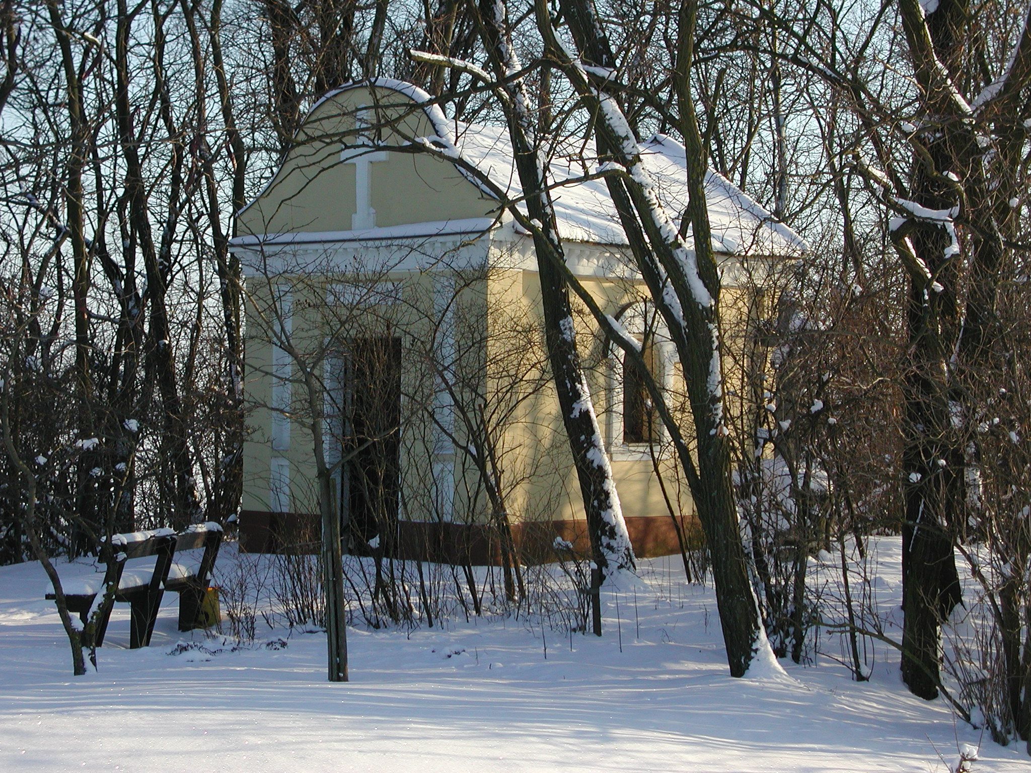 Eine kleine Kapelle im Winter, umgeben von schneebedeckten Bäumen.