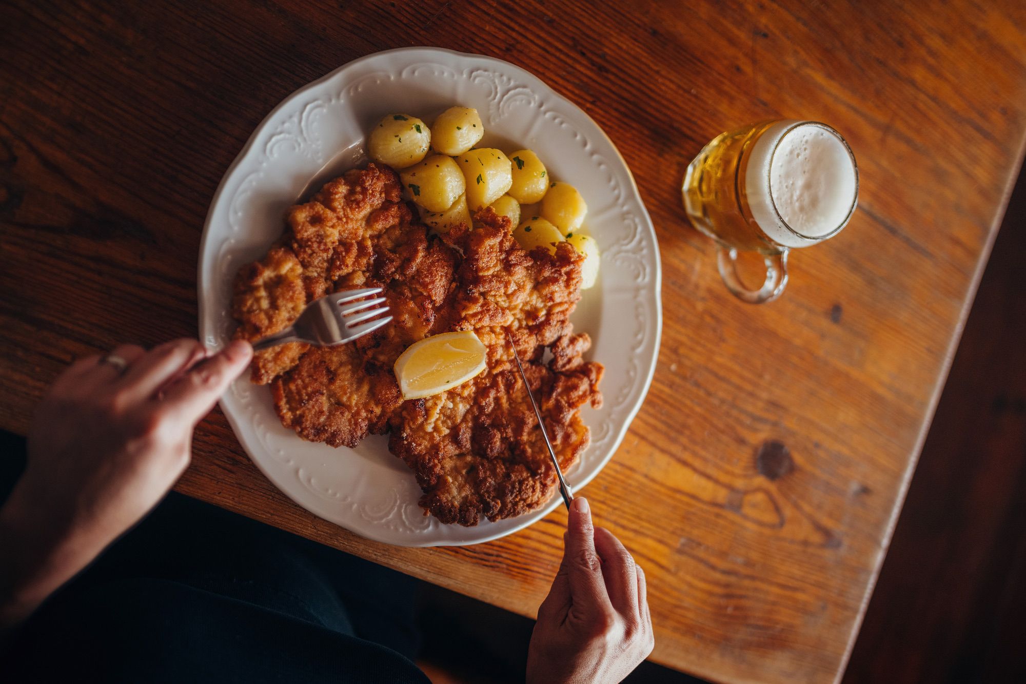 Teller mit Schnitzel, Kartoffeln und Zitrone, daneben ein Glas Bier.