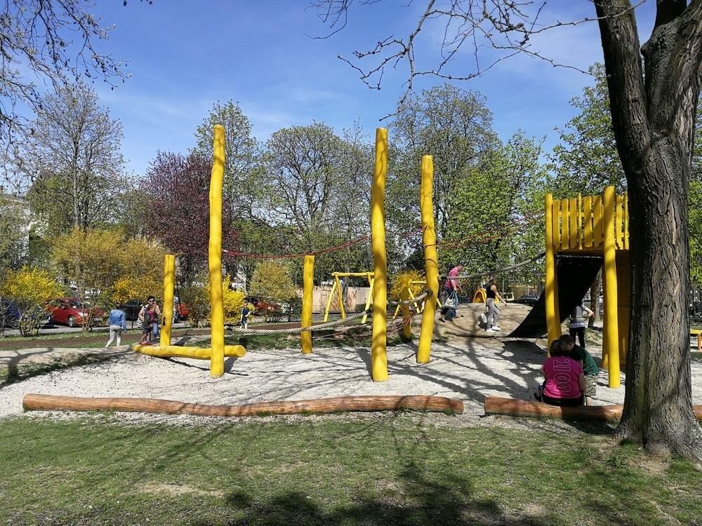 Spielplatz mit gelben Holzelementen und Kindern beim Spielen.