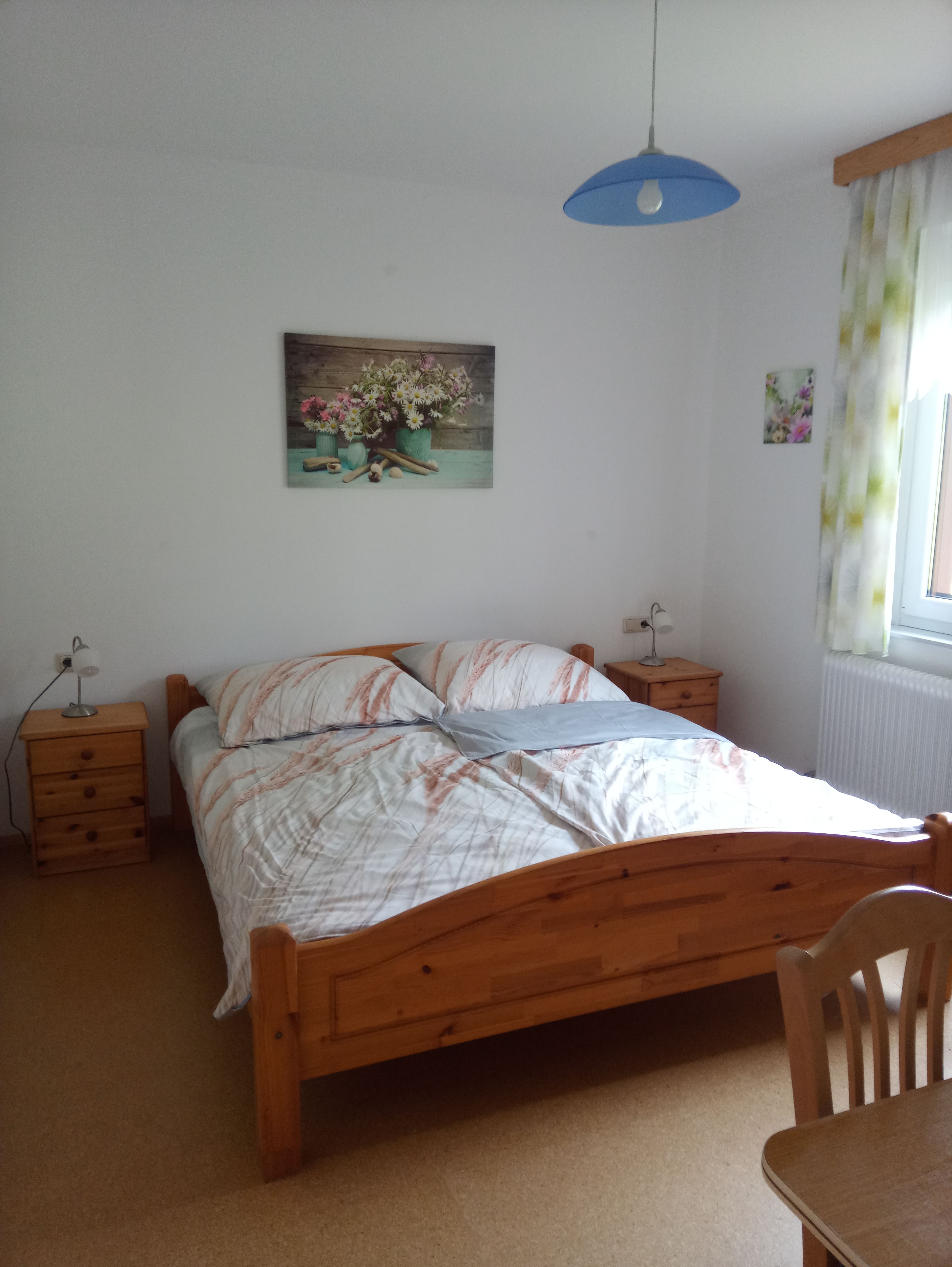 Schlafzimmer mit Holzbett, Nachttischen und Blumenbildern an der Wand.