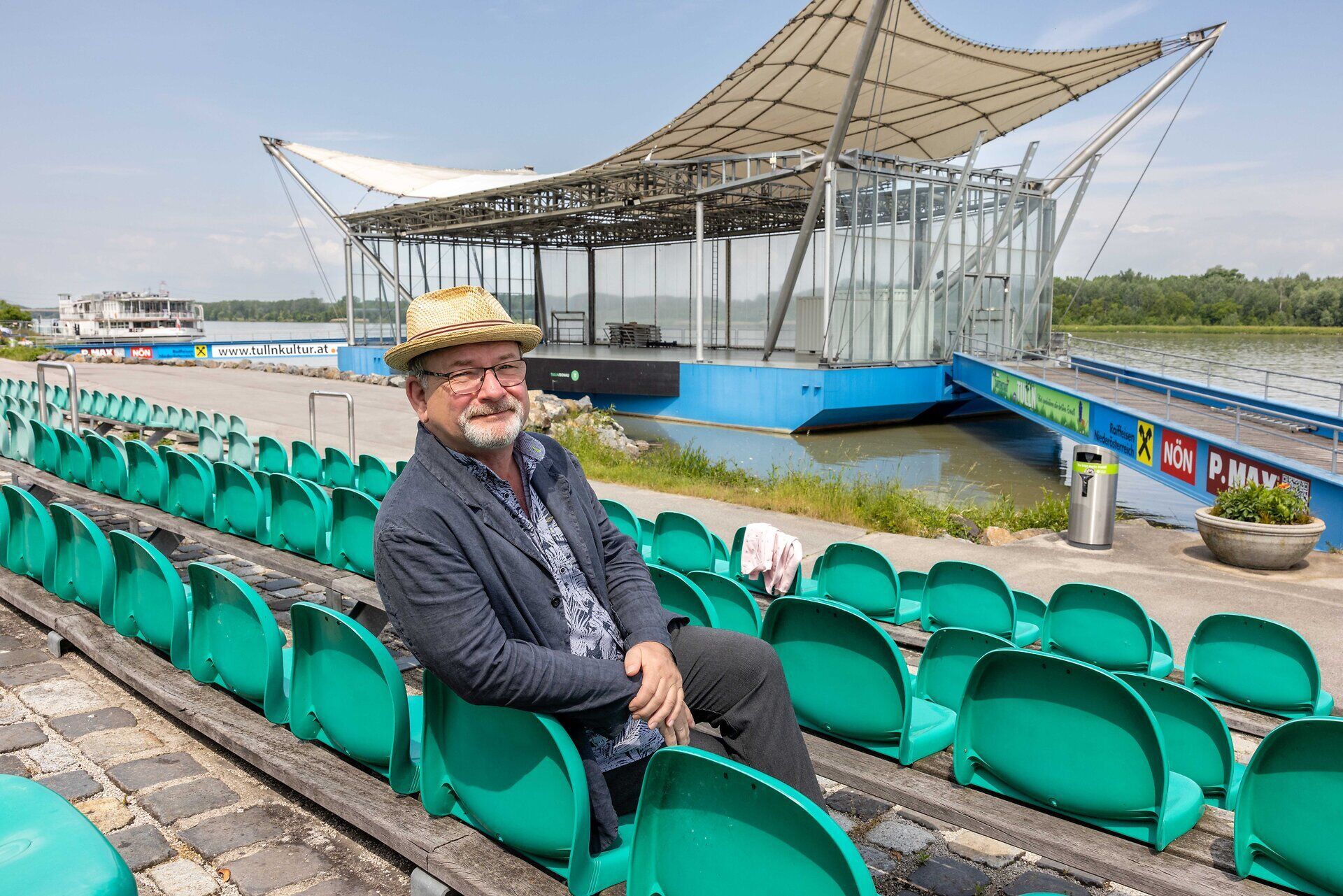 Mann sitzt auf den Bänken der Donaubühne, im Hintergrund die Bühne, ein Schiff und die Donau