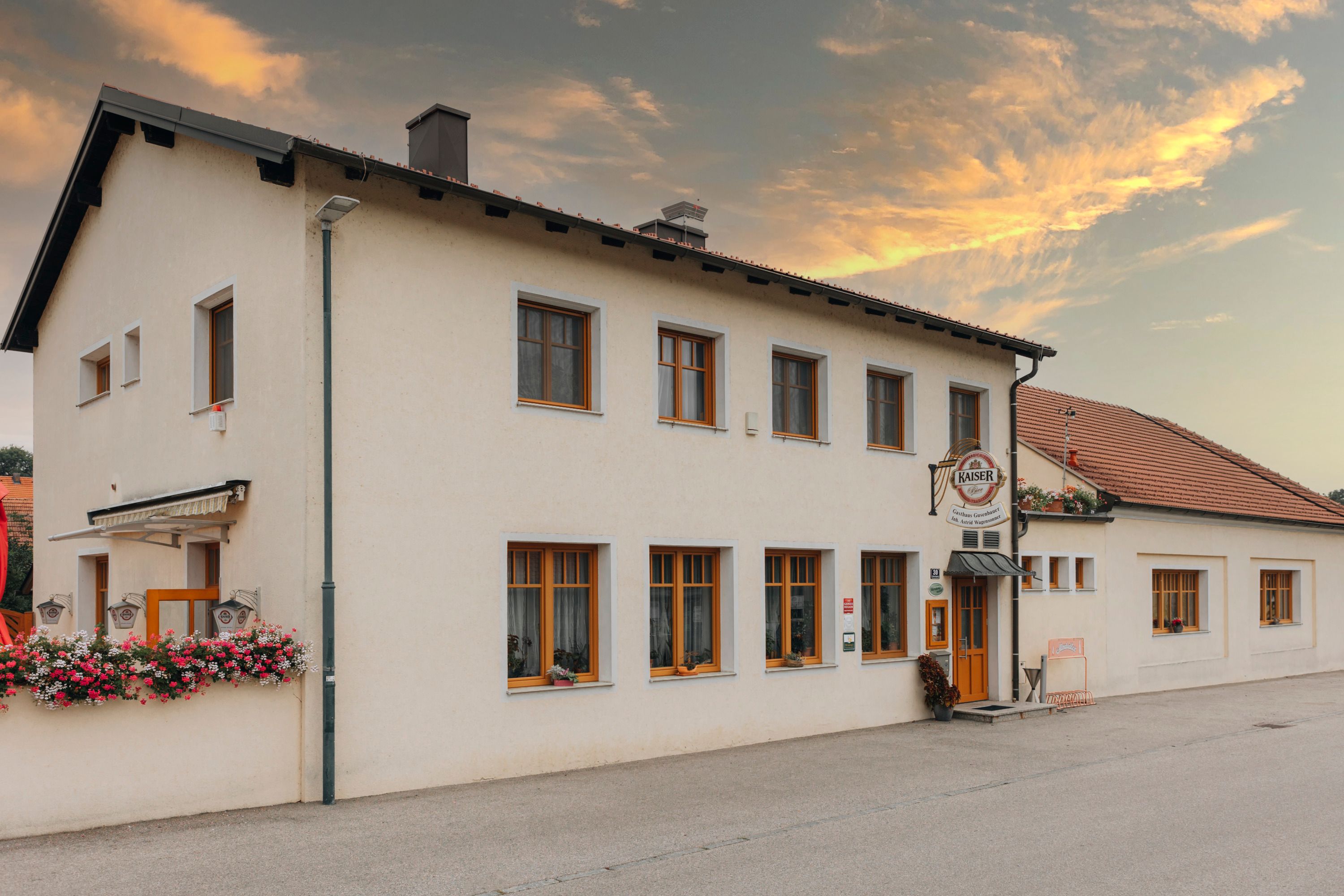 Gasthaus mit Blumenschmuck und Kaiser-Bierschild bei Sonnenuntergang.