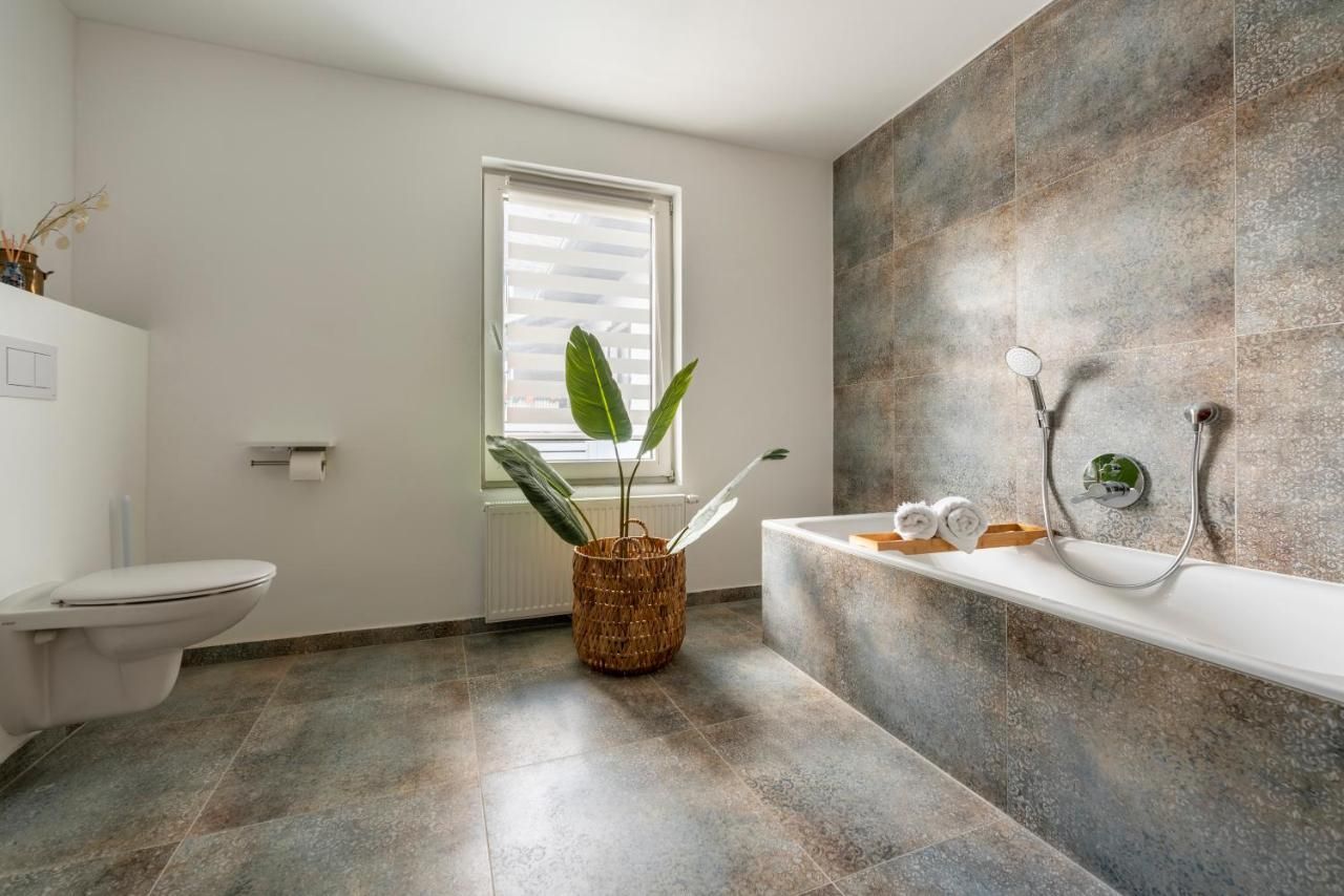 Modernes Badezimmer mit Badewanne, Pflanze und Fenster.