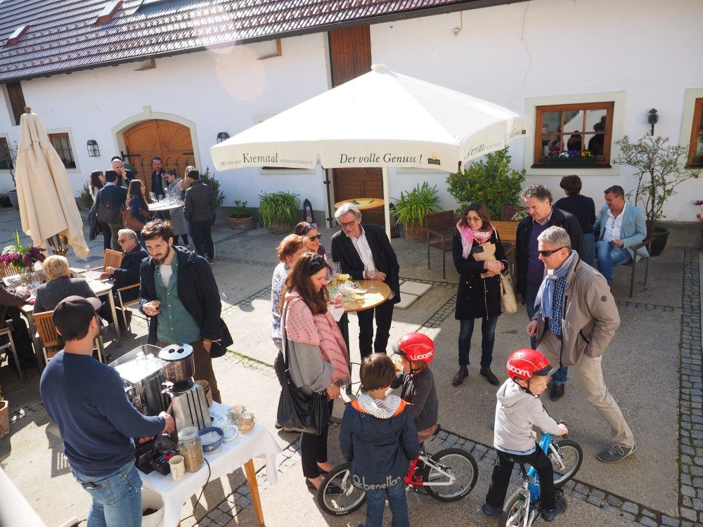 Menschen bei einem Frühlingsfest in einem Hof mit Sonnenschirm und Getränken.