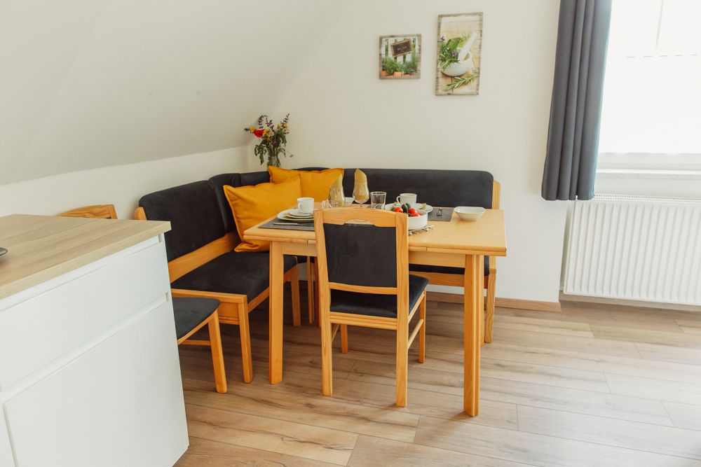 Essbereich mit Holztisch, Stühlen und Eckbank, gedeckt mit Geschirr, Blumenstrauß und Dekoration an der Wand.