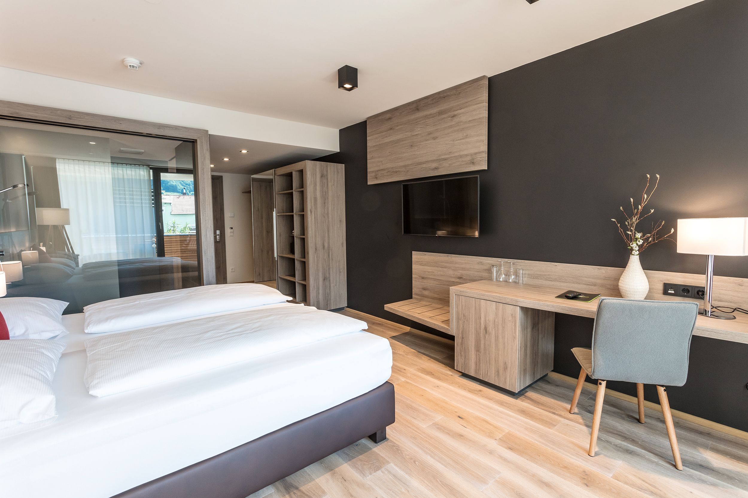 Modern eingerichtetes Hotelzimmer mit Doppelbett, Schreibtisch, Stuhl und Flachbildfernseher an der Wand.