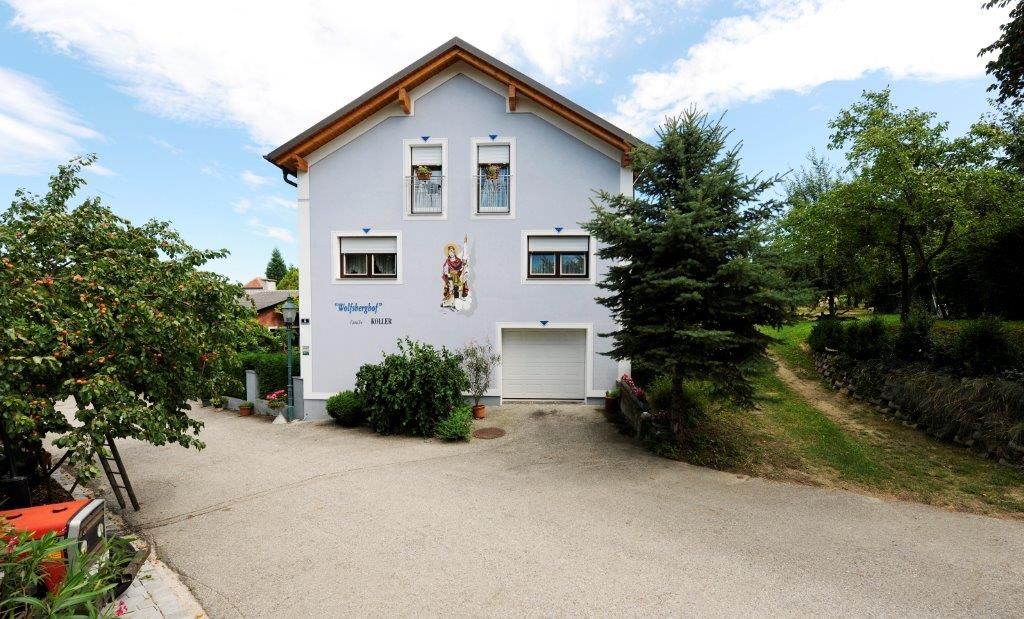 Ein zweistöckiges Haus mit blauer Fassade und Holzdach, umgeben von Bäumen und einem gepflasterten Weg.