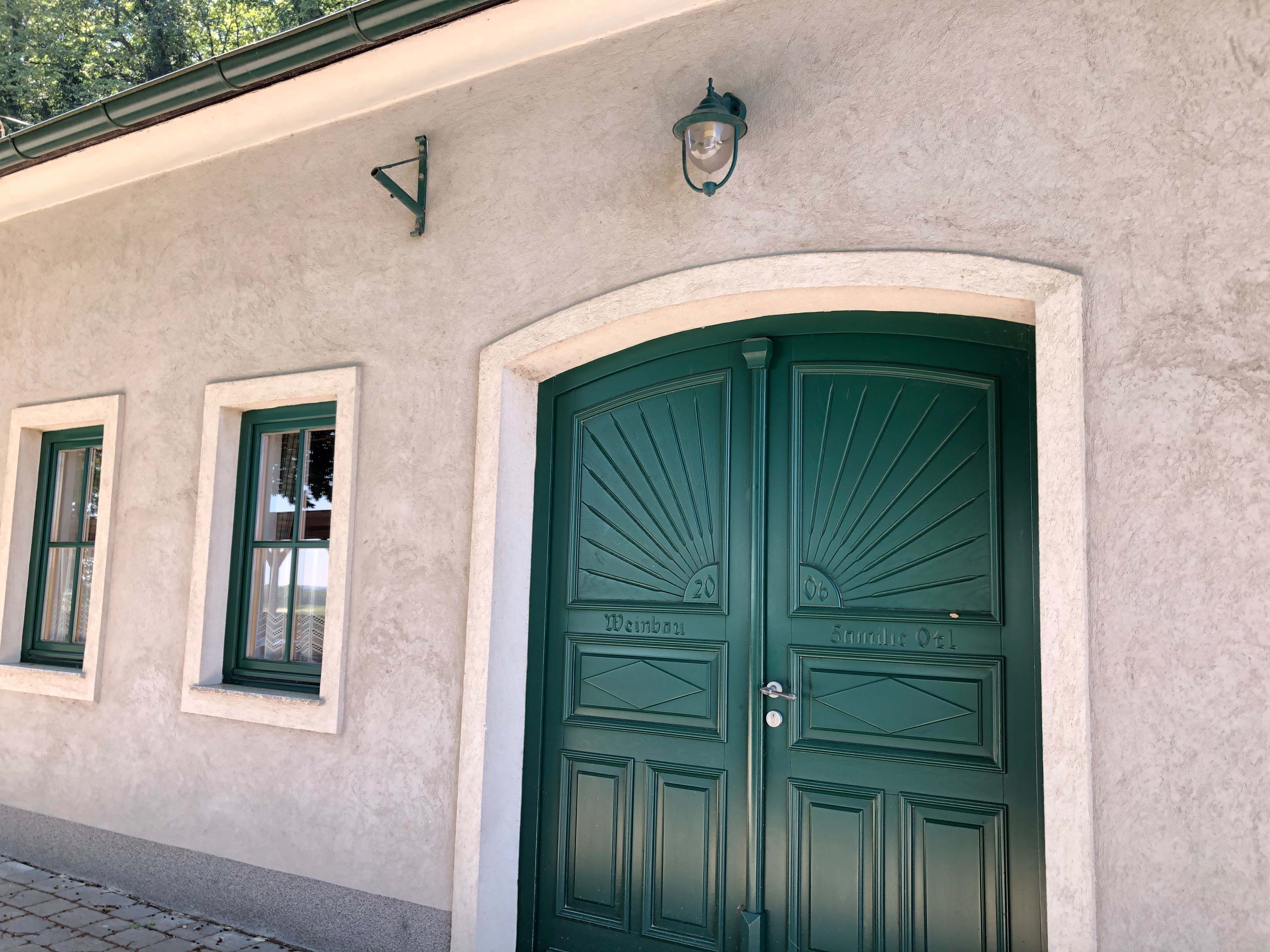 Grünes Tor und Fenster eines Heurigen mit beiger Fassade.
