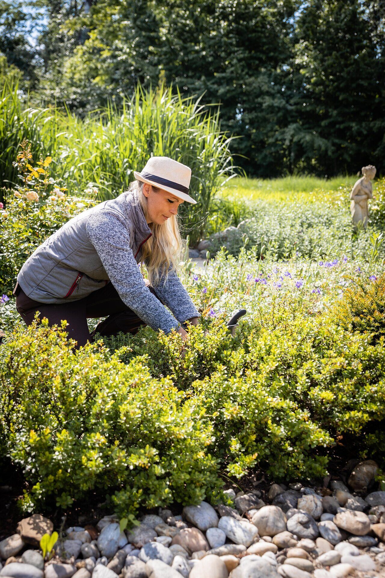 Eine Frau bei der Gartenarbeit zwischen dicht bepflanzten Beeten.