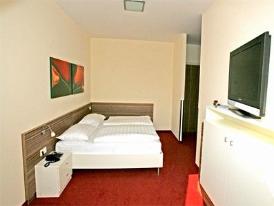 Ein Hotelzimmer mit Doppelbett, rotem Teppichboden und Flachbildfernseher an der Wand.