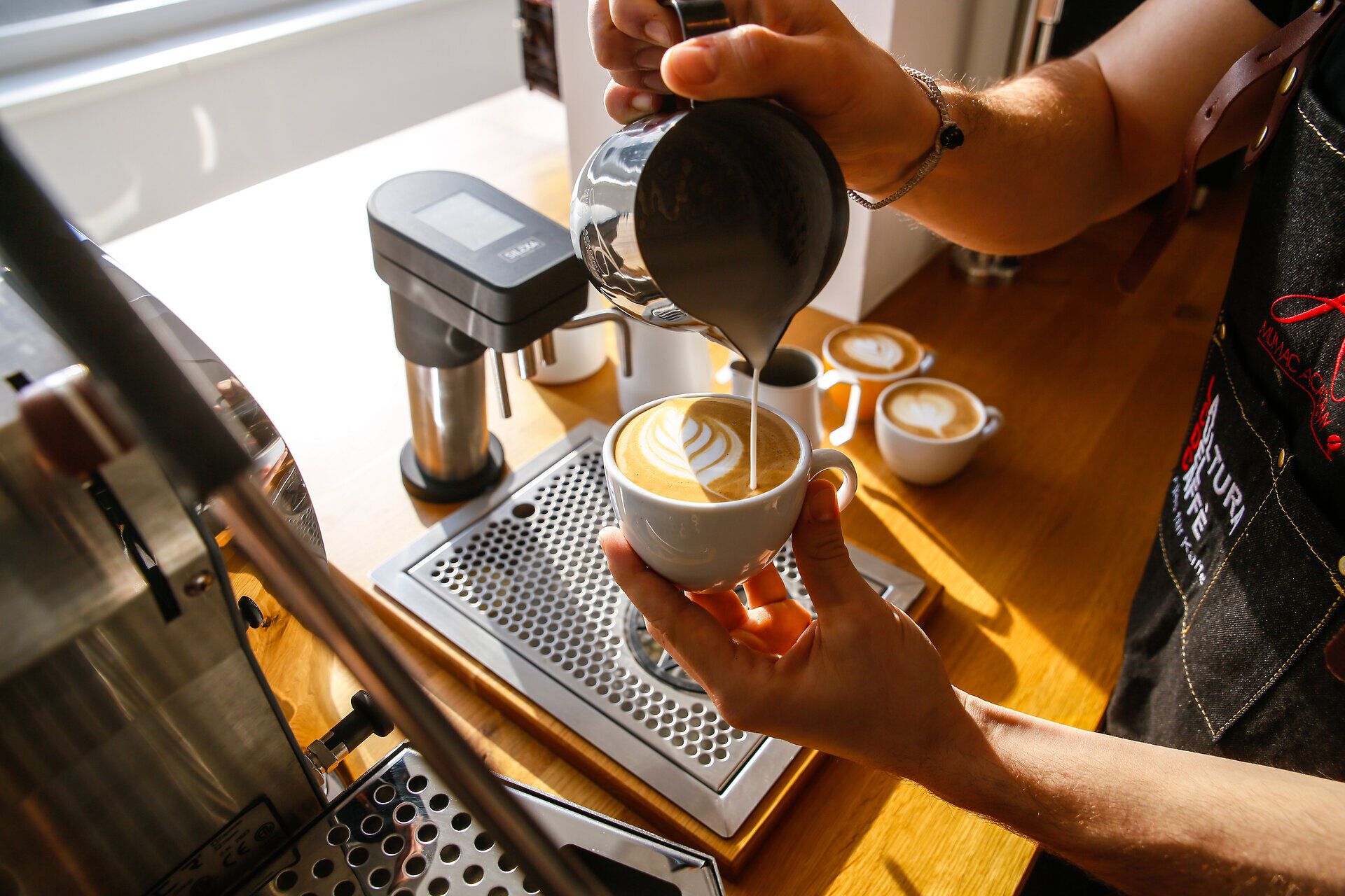 In einem einladenden Café wird mit viel Geschick ein perfekter Cappuccino zubereitet. Die kunstvolle Latte-Art auf der cremigen Oberfläche verspricht ein Geschmackserlebnis, das die Sinne verzaubert. Hier trifft sich die Leidenschaft für Kaffee mit einem gemütlichen Ambiente, ideal für eine entspannte Auszeit.