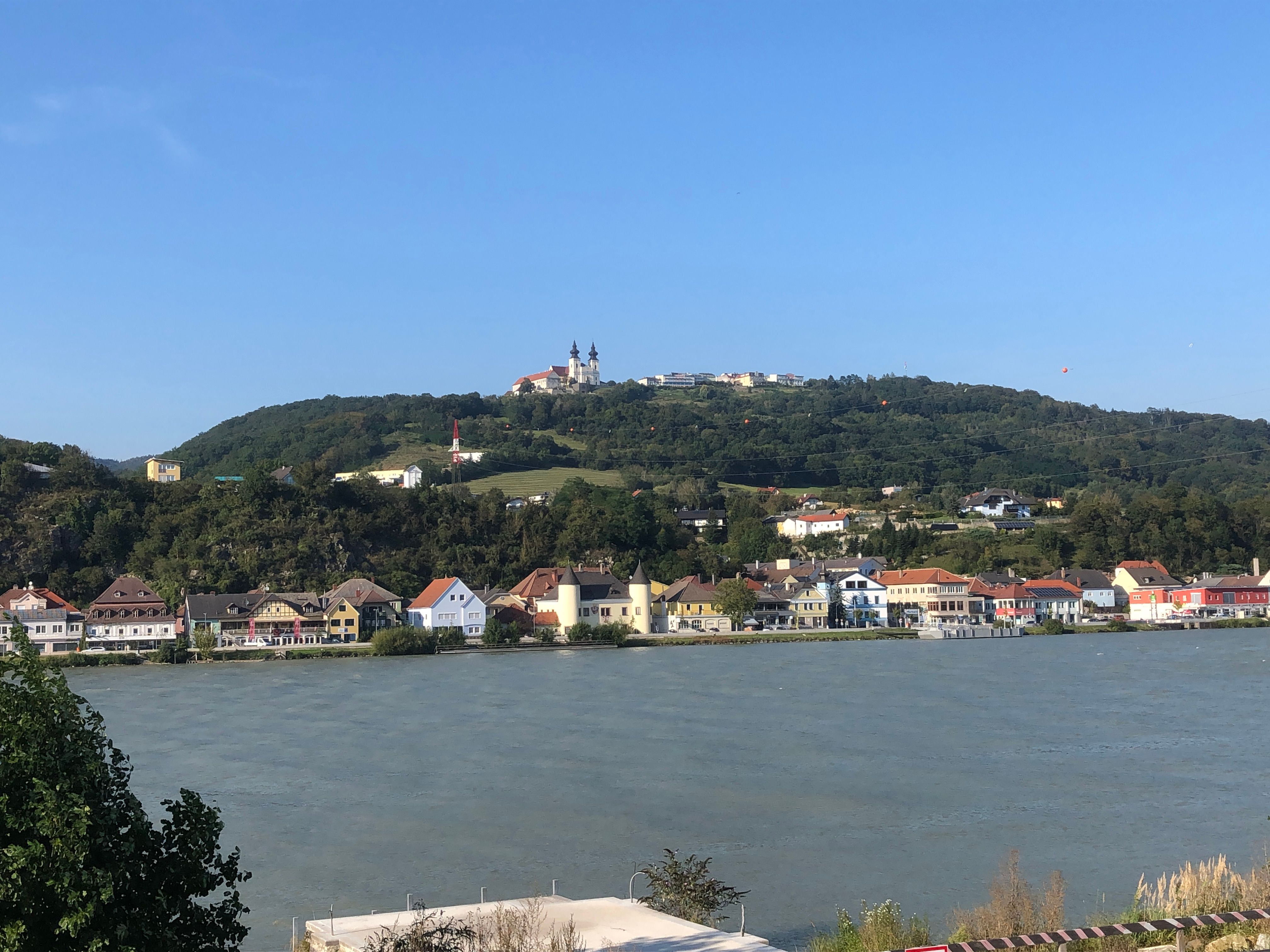 Blick auf die Basilika Maria Taferl auf einem Hügel, mit Häusern und einem Fluss im Vordergrund.