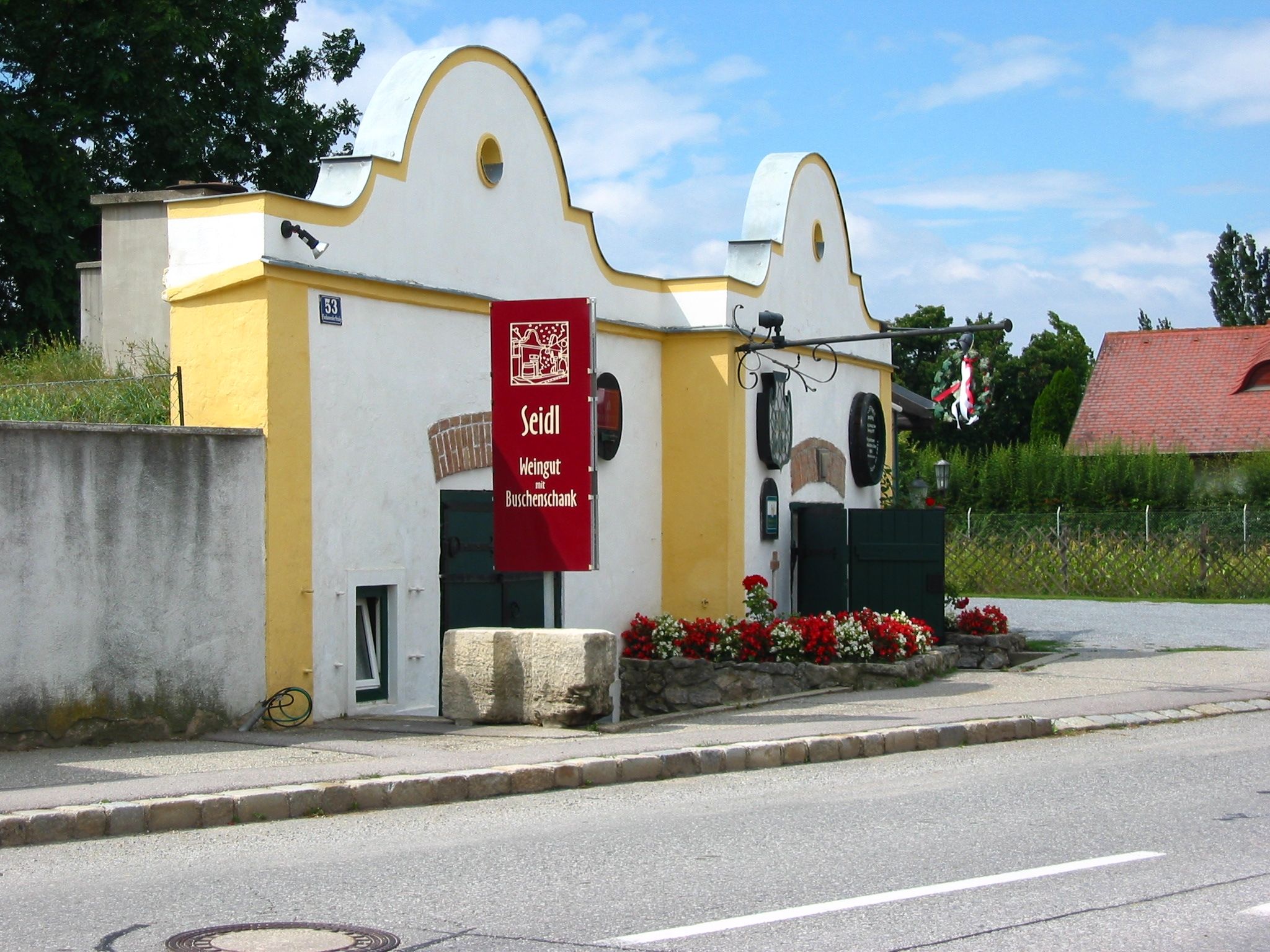 Weingut Seidl mit gelbem Gebäude und rotem Schild.