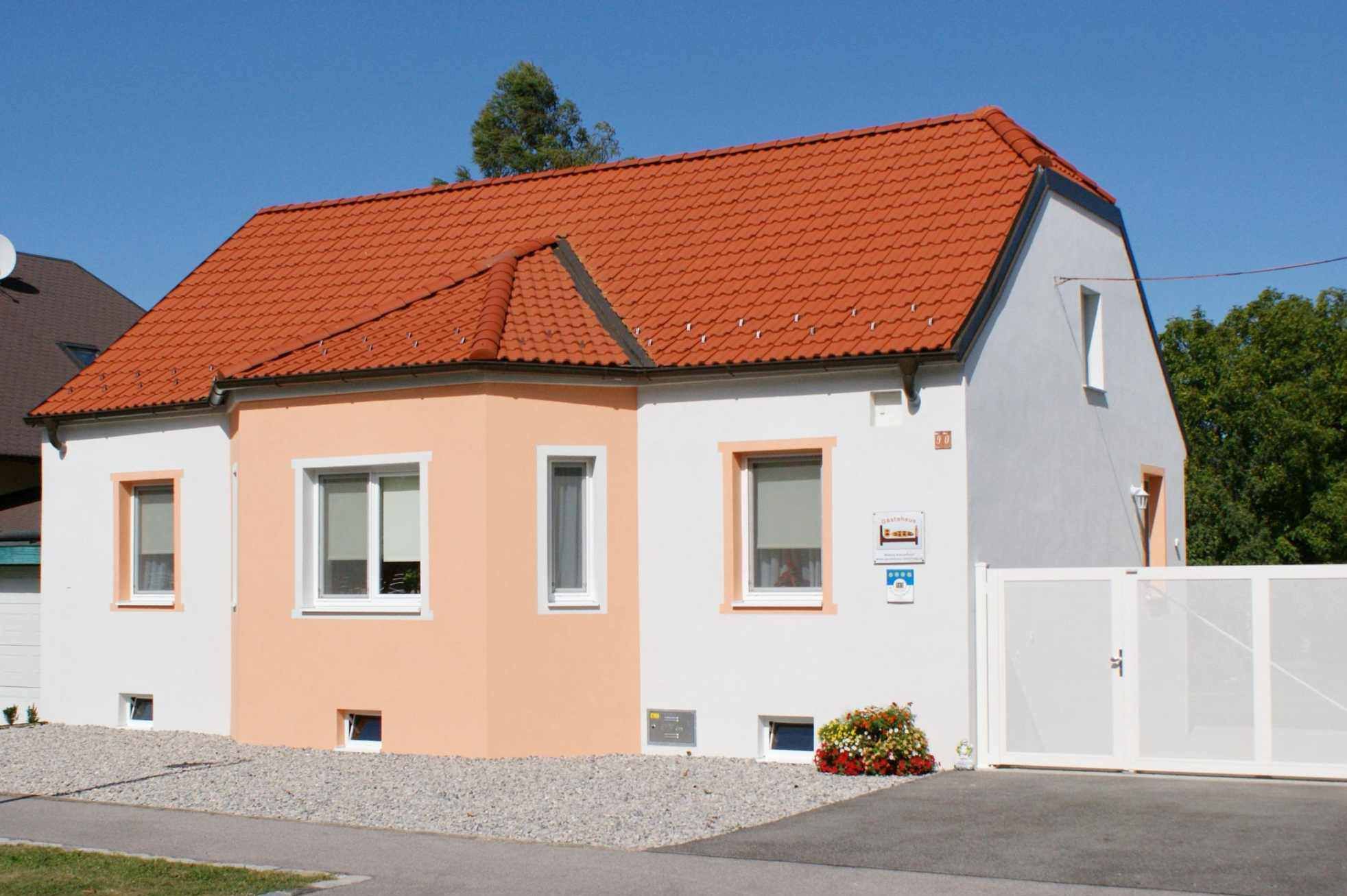 Malý jednopatrový dům s oranžovou střechou a bílou fasádou pod modrou oblohou.