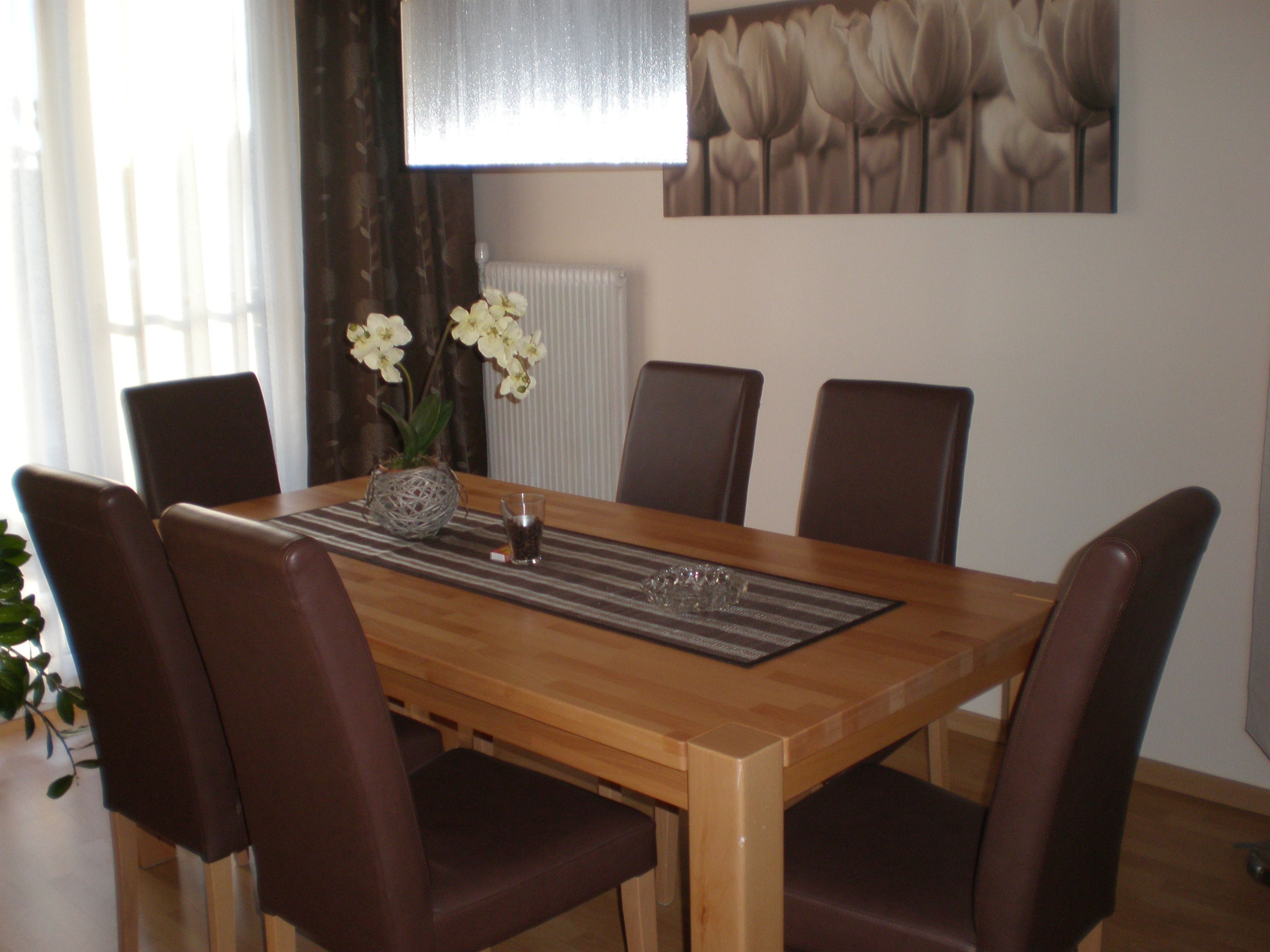 Esszimmer mit Holztisch, sechs braunen Stühlen und Orchidee als Dekoration.