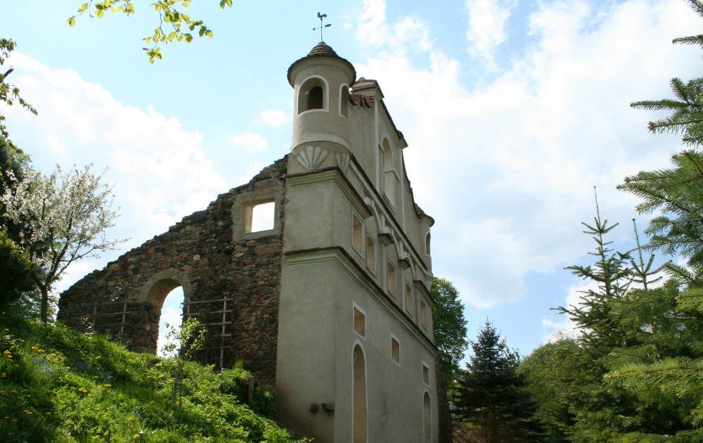 Ruine eines Schlosses mit erhaltenem Turm und Mauerresten, umgeben von Bäumen und blauem Himmel.