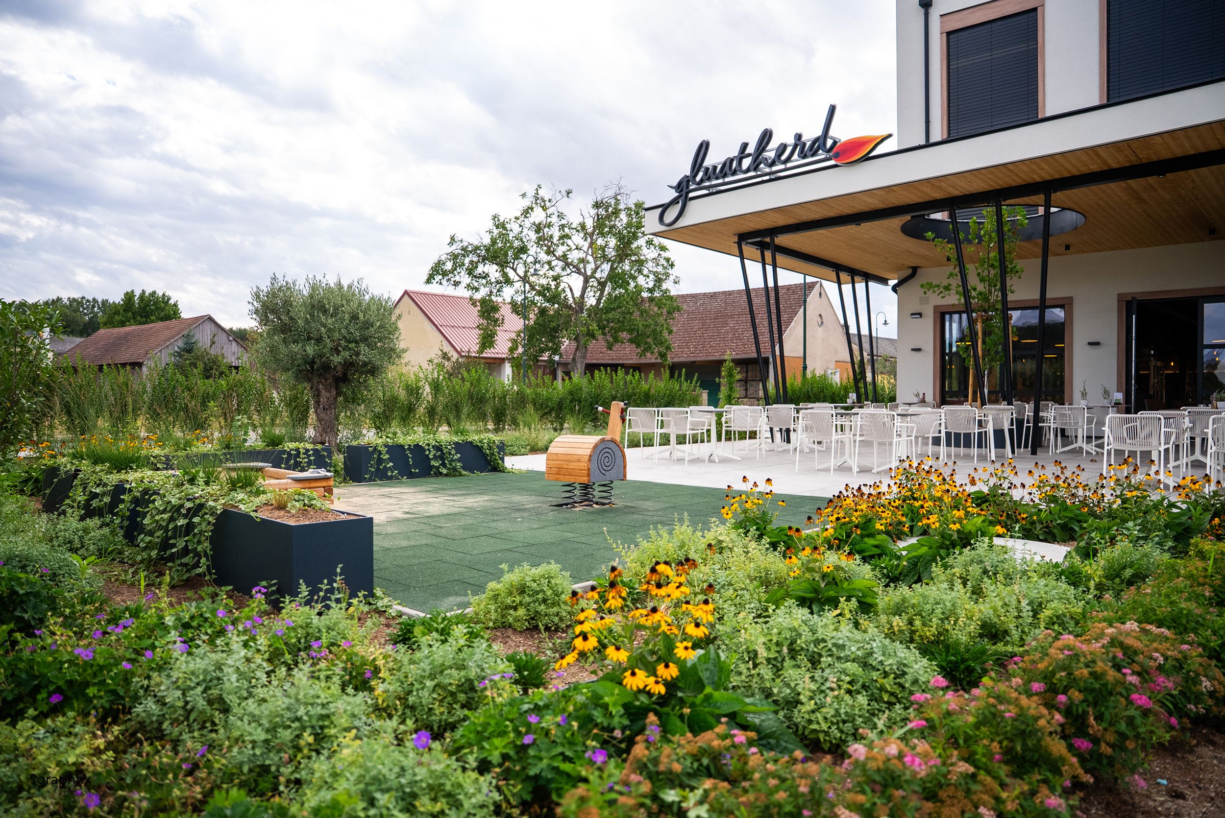 Außenbereich eines Restaurants mit Kinderspielplatz sowie Tische und Sesseln.