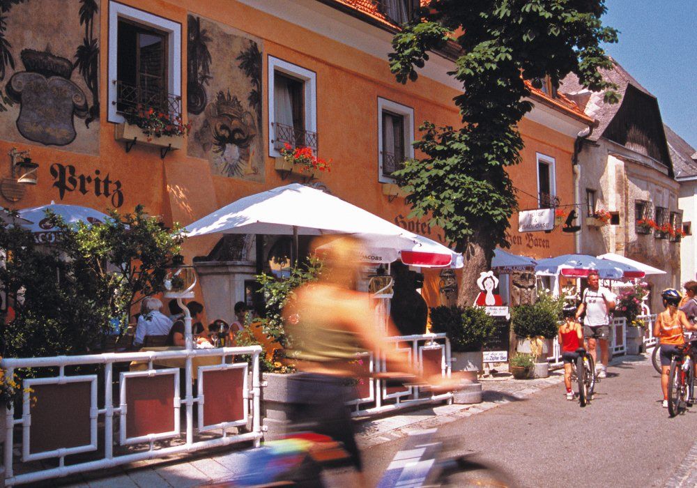 Radfahrer vor einem Hotel mit Terrasse und Sonnenschirmen.