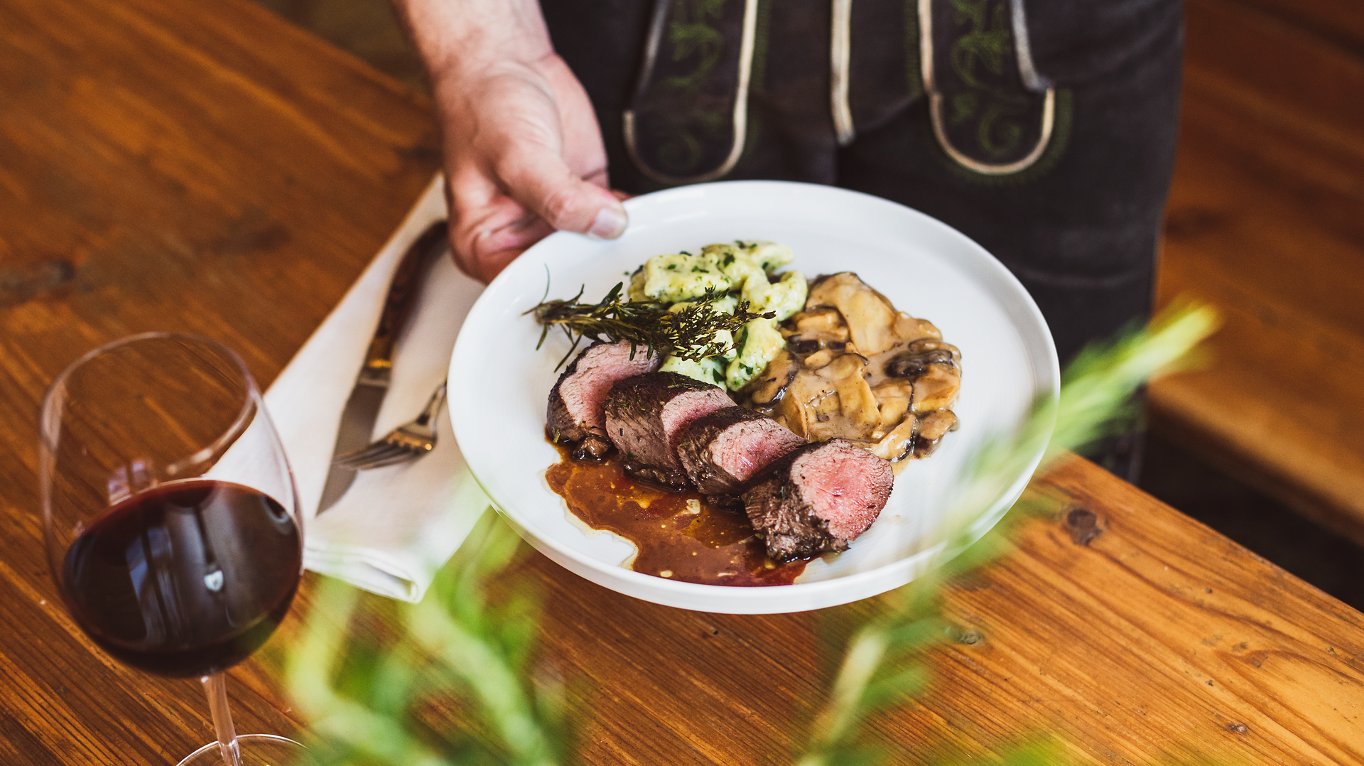 Ein köstliches Hirschfilet, perfekt zubereitet und liebevoll angerichtet, lädt zu einem genussvollen Abendessen ein. Die zarten Spätzle und die aromatischen Pilze ergänzen das Gericht harmonisch und versprechen ein unvergessliches Geschmackserlebnis. Ein Glas Rotwein rundet das kulinarische Erlebnis ab und schafft eine einladende Atmosphäre.