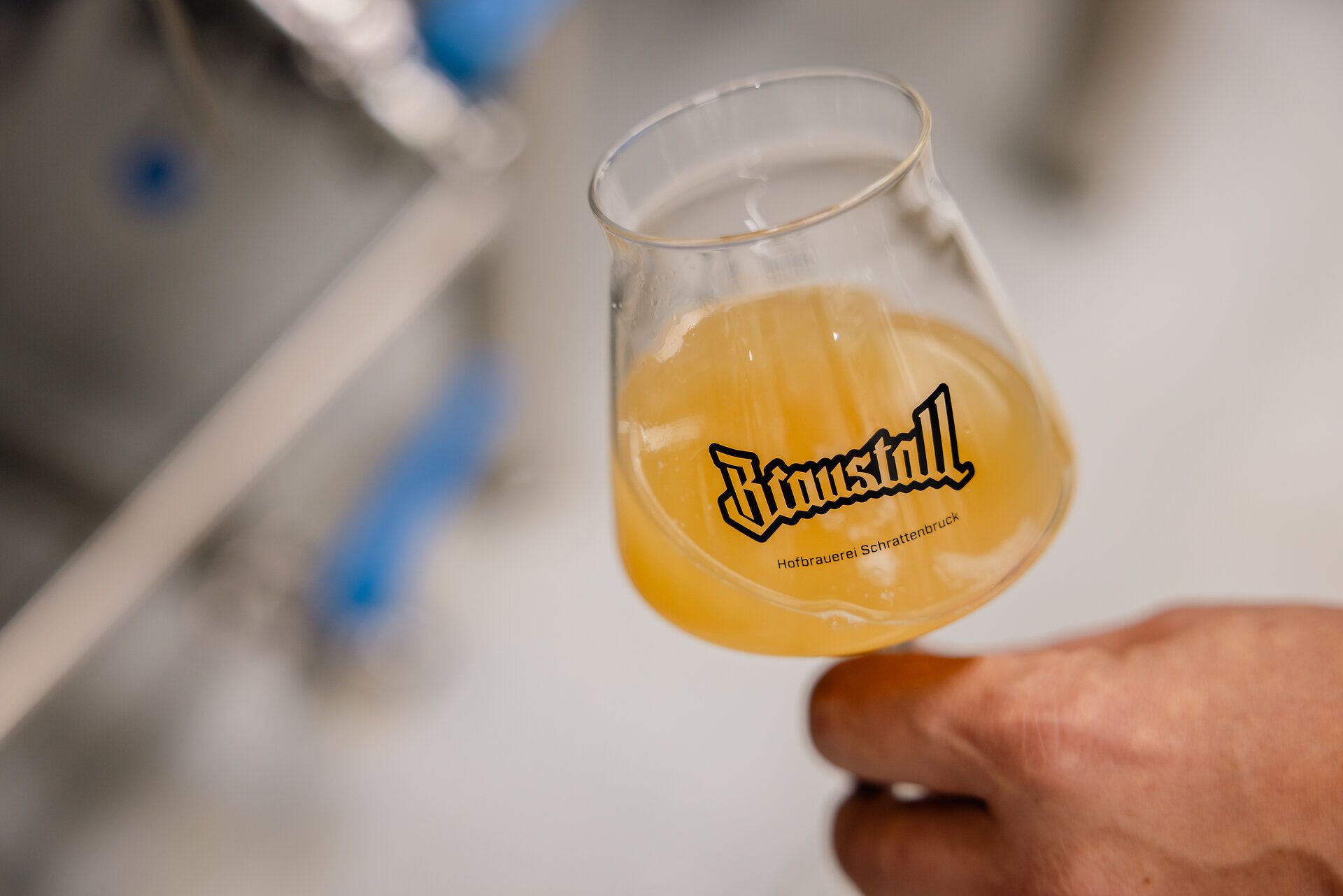 Glas mit hellem Bier und Braustall-Logo.